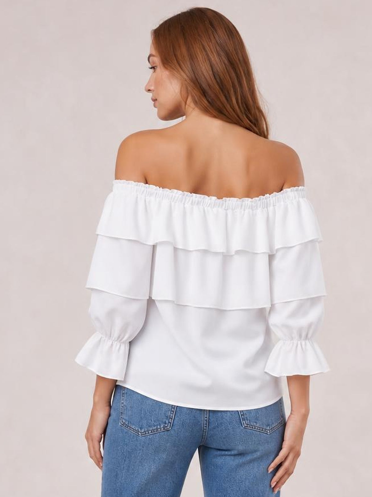 A model turned away wears a white off-shoulder blouse with layered ruffles, flounce sleeves, gathered neckline, and a relaxed silhouette.