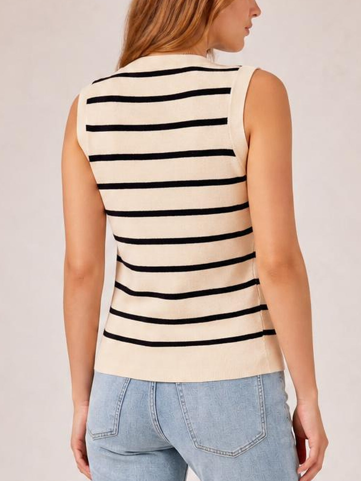 A model turned slightly away wears a cream knit tank with black horizontal stripes, sleeveless construction, and a fitted silhouette that falls to the hips.