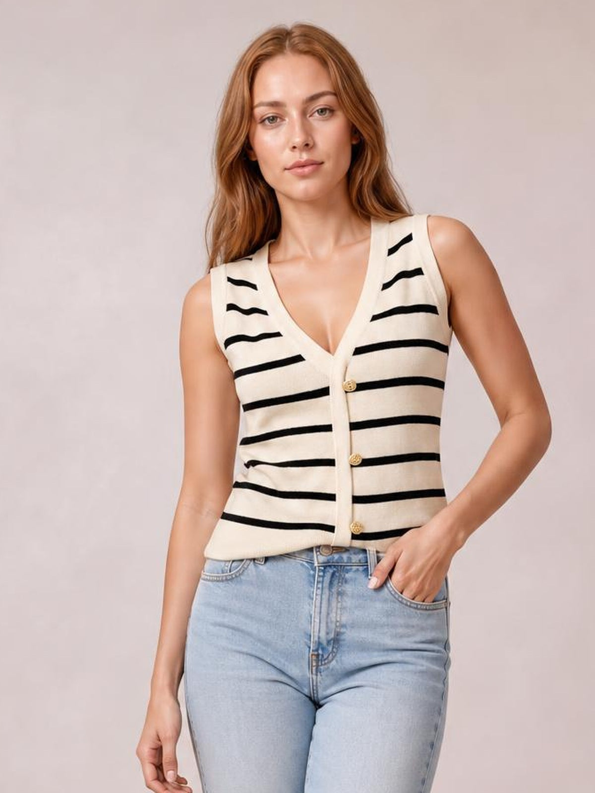 Model wears an ivory and black striped V-neck knit tank with a fitted sleeveless silhouette, button-front construction, and one hand in her jeans pocket.