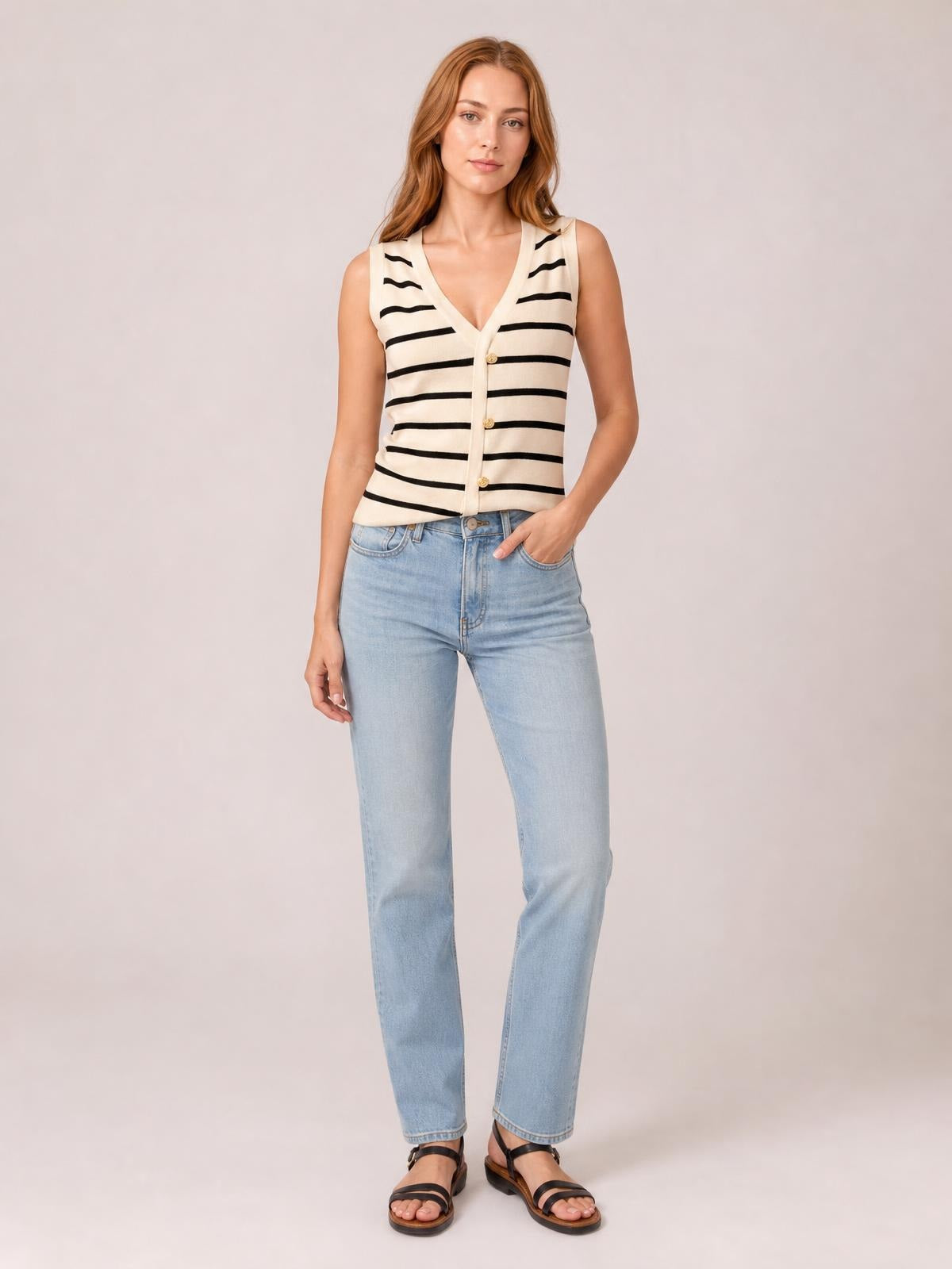 Model poses in a striped cream-and-black V-neck knit tank with button front, sleeveless silhouette, and straight hem, paired with light-wash jeans.
