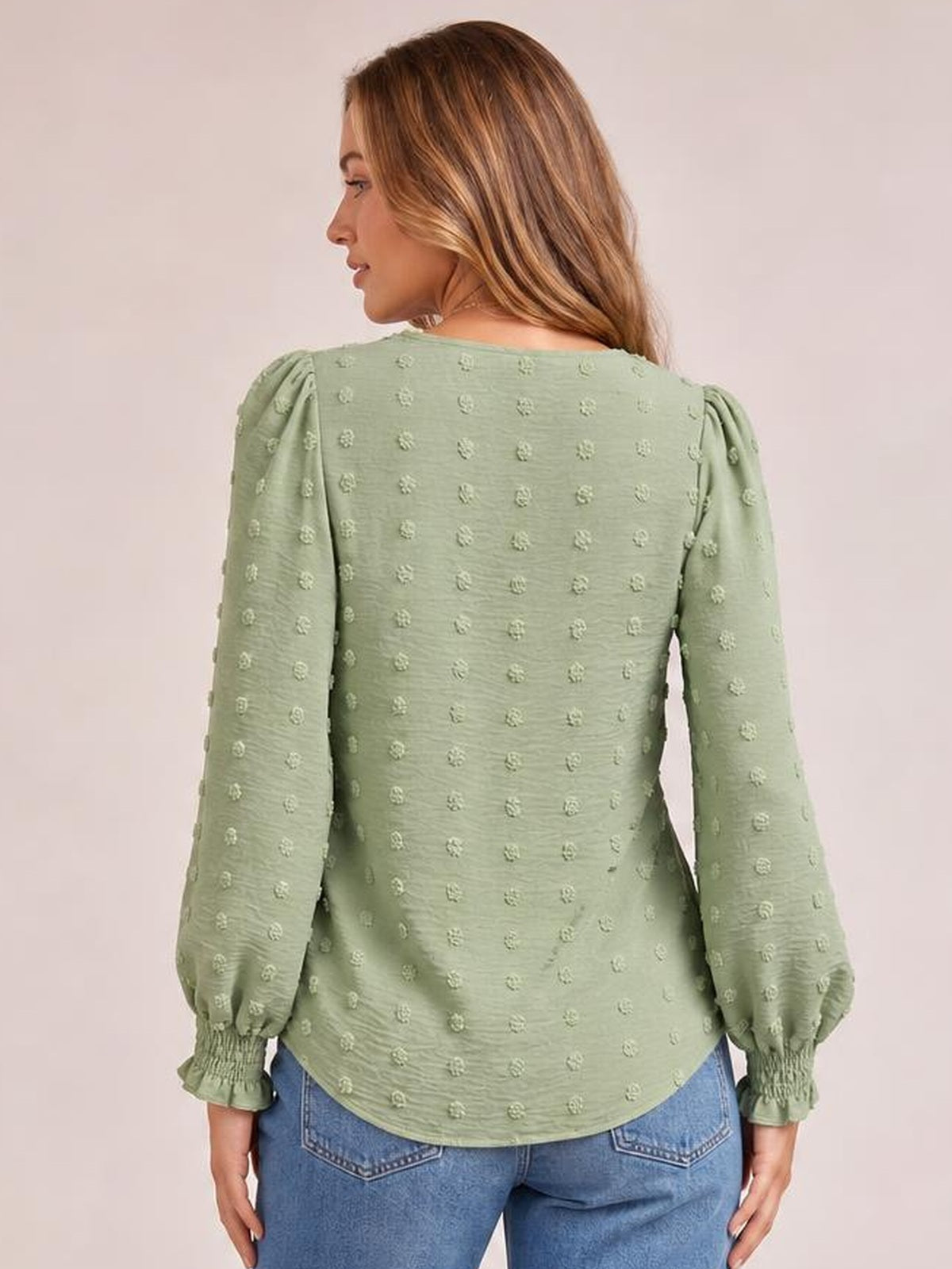 Model shown from behind wearing a sage green Swiss dot blouse with long puff sleeves, gathered cuffs, a relaxed silhouette, and curved hem.