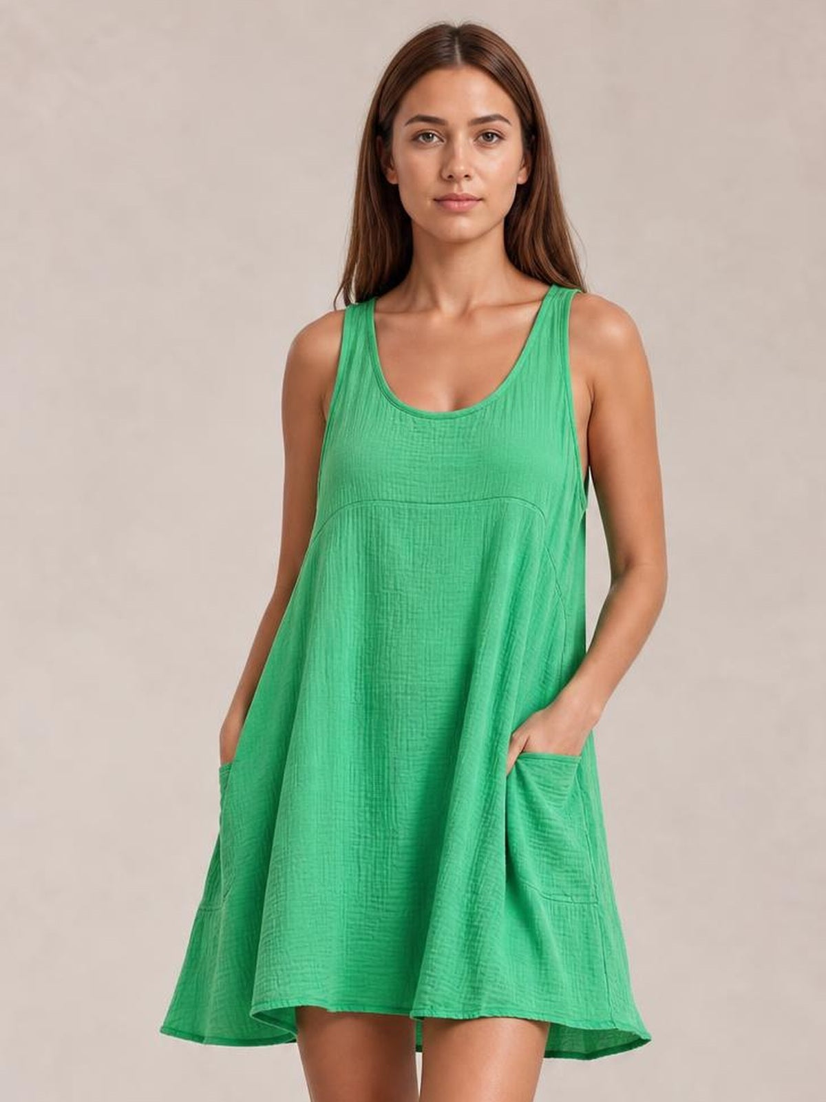 A model poses in a bright green scoop-neck mini dress with wide straps, a loose A-line silhouette, under-bust seam, and side pockets, holding her hands inside them.