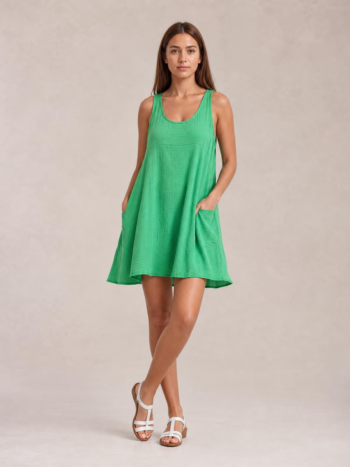 Model wears a green tied scoop-neck mini dress with wide straps, a relaxed A-line silhouette, visible seam detail, and side pockets, posing with crossed legs.
