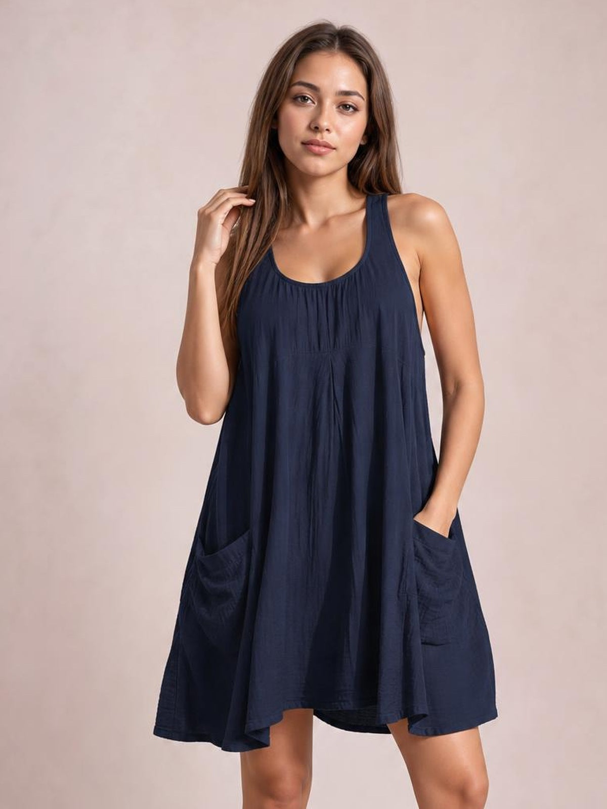 Model poses in a navy wide-strap scoop-neck mini dress with a loose, flowing silhouette, vertical gathers, and oversized patch pockets.