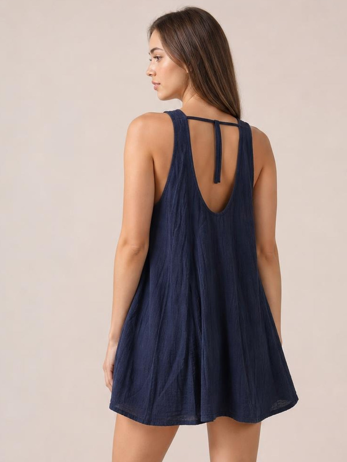 A model shows the back of a navy tied scoop-neck mini dress with wide straps, a low scoop back, center tie detail, and a flowing A-line silhouette.