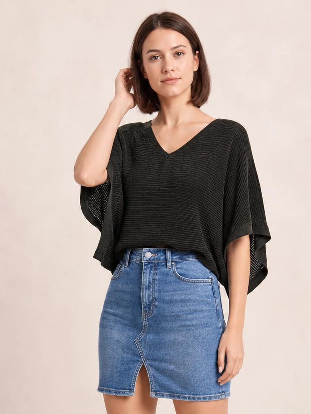 Model wears a black V-neck batwing sleeve knit top with a loose draped silhouette, textured horizontal knit, and relaxed cuffed sleeve edges.