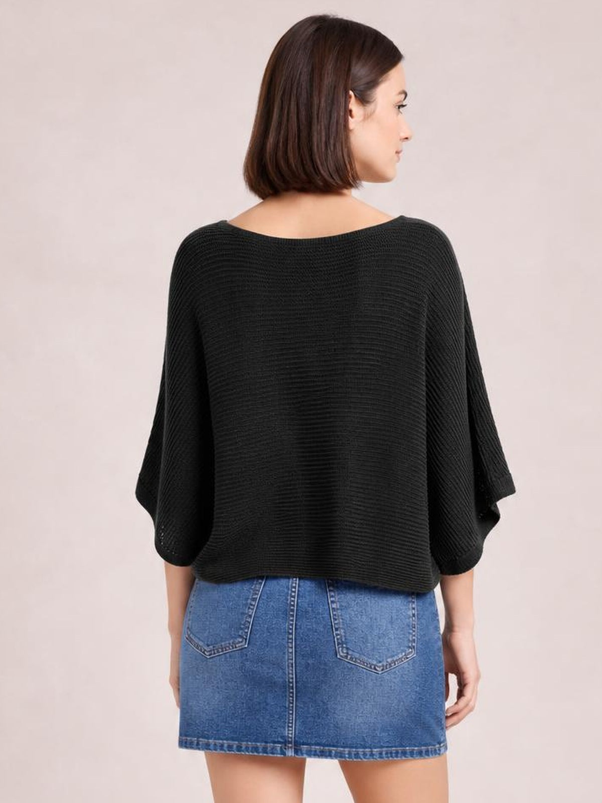 Model shown from behind wearing a black batwing-sleeve knit top with a wide neckline, textured ribbed construction, and a loose, boxy hip-length silhouette.