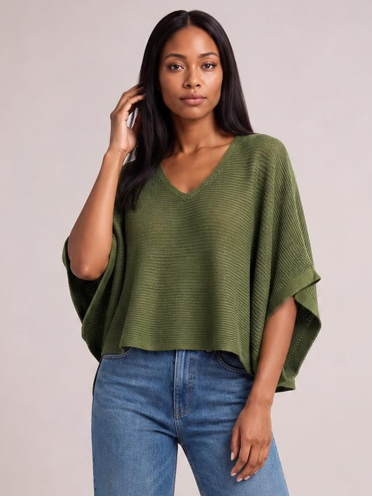 Model poses in a moss-green V-neck batwing sleeve knit top with a relaxed, draped silhouette, wide sleeves, and a cropped hem.