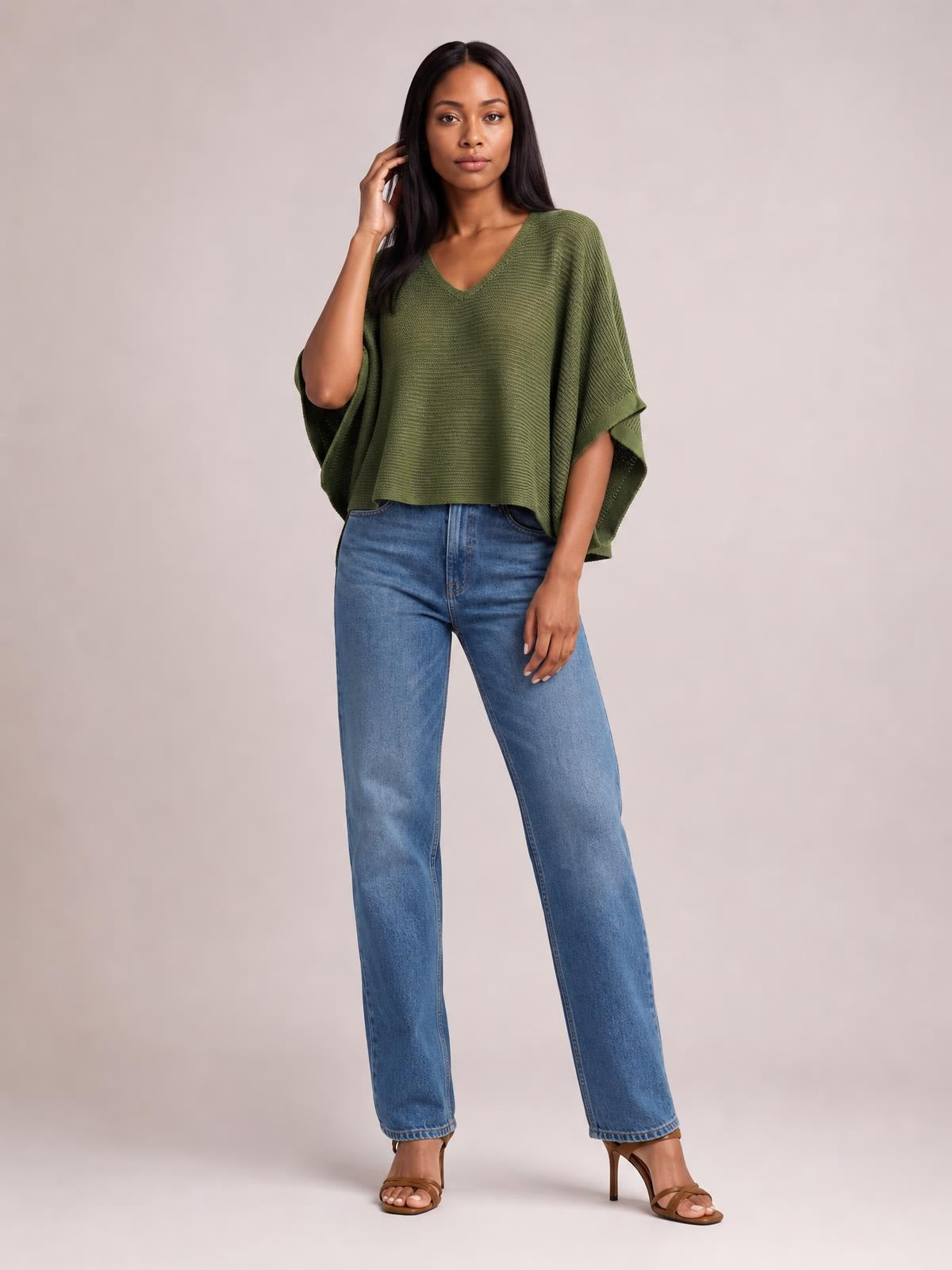Model wearing an olive green V-neck batwing sleeve knit top with a relaxed draped silhouette and wide cropped hem, paired with blue jeans.