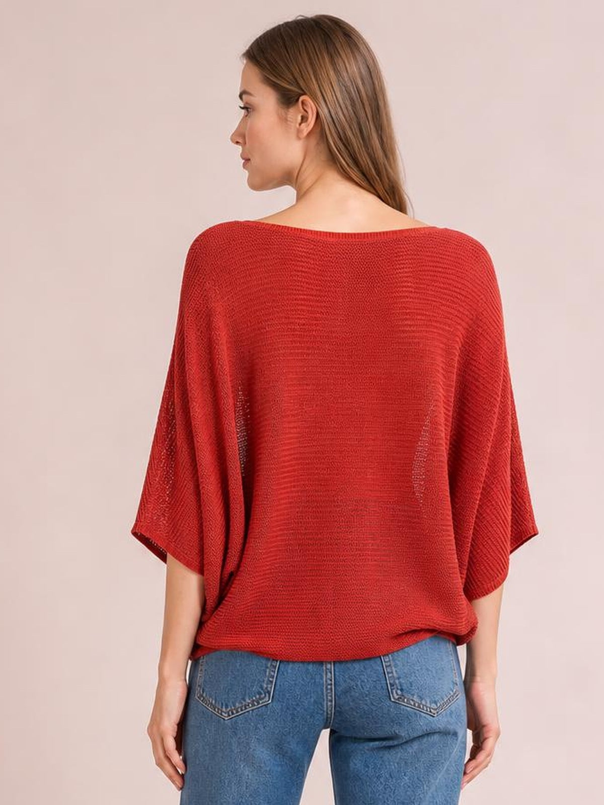 A model stands in a loose red knit top with wide batwing sleeves, a relaxed silhouette, and a softly textured open-knit construction.