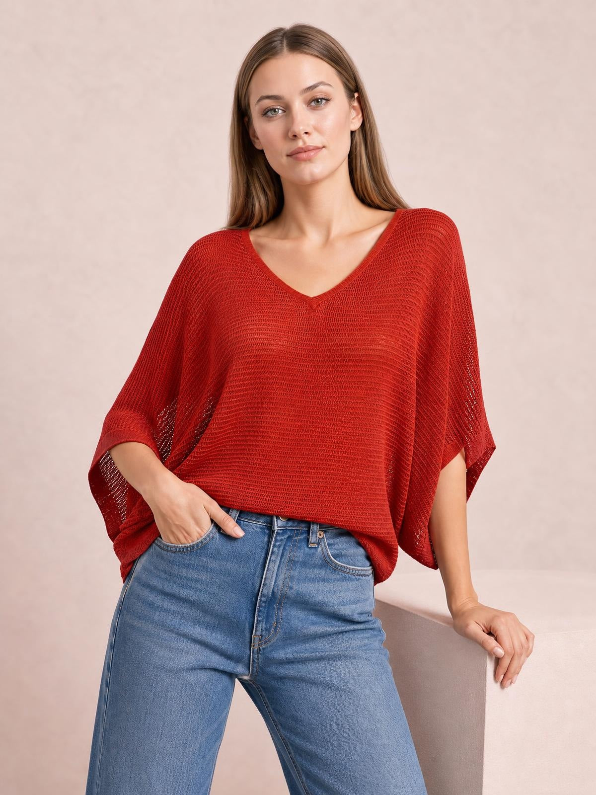 Model wearing a red V-neck batwing sleeve knit top with a loose, draped silhouette and open-knit texture, paired with blue jeans.