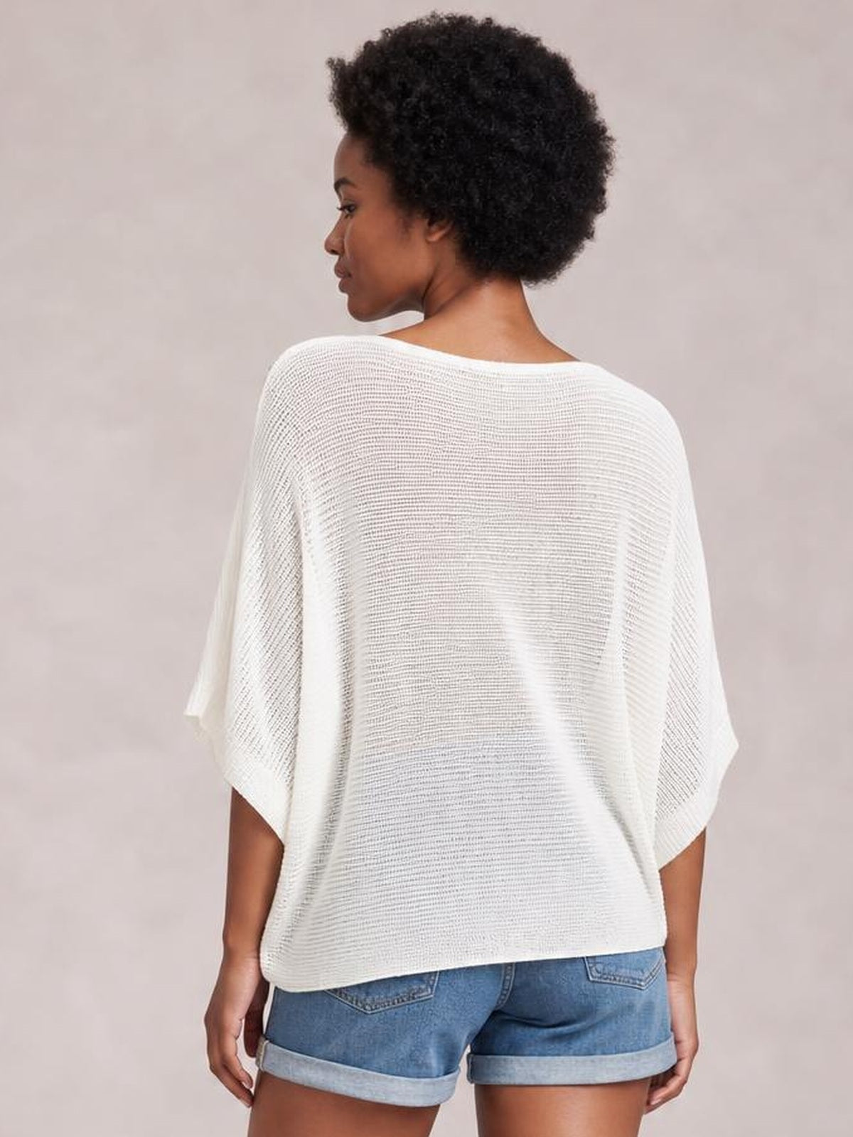 Model shown from the back wearing a white V-neck batwing sleeve knit top with a loose, flowing silhouette and wide sleeves.