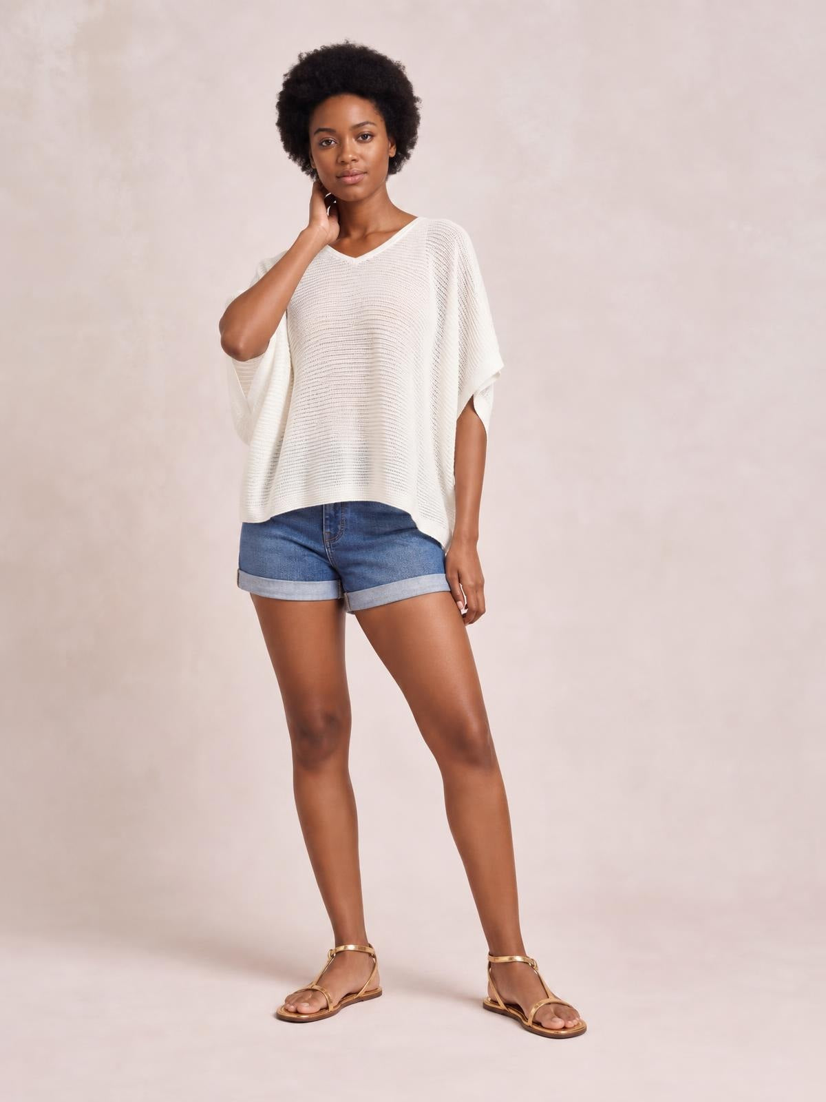 Model wears a white V-neck batwing sleeve knit top with an open-knit texture and loose, relaxed silhouette, standing with one hand at her neck.