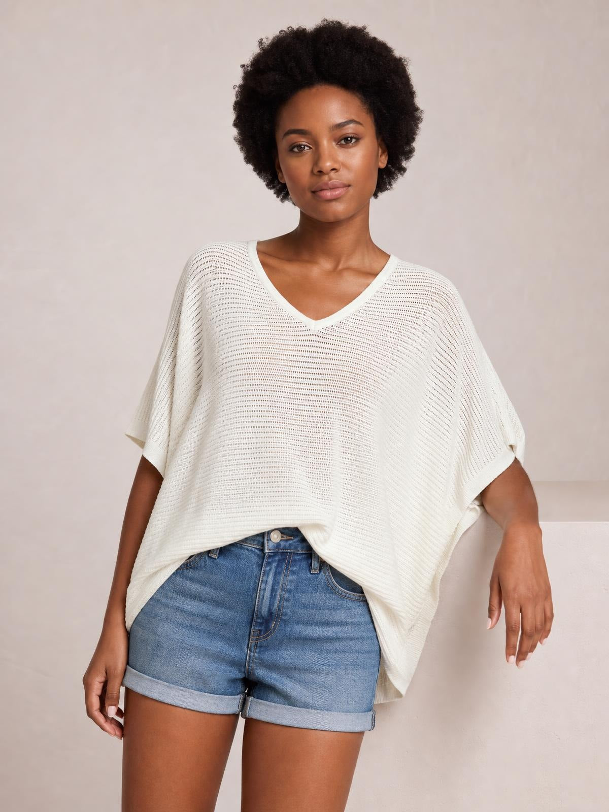 Model wearing an ivory V-neck batwing sleeve knit top with a loose, draped silhouette, wide short sleeves, and a textured open-knit construction.