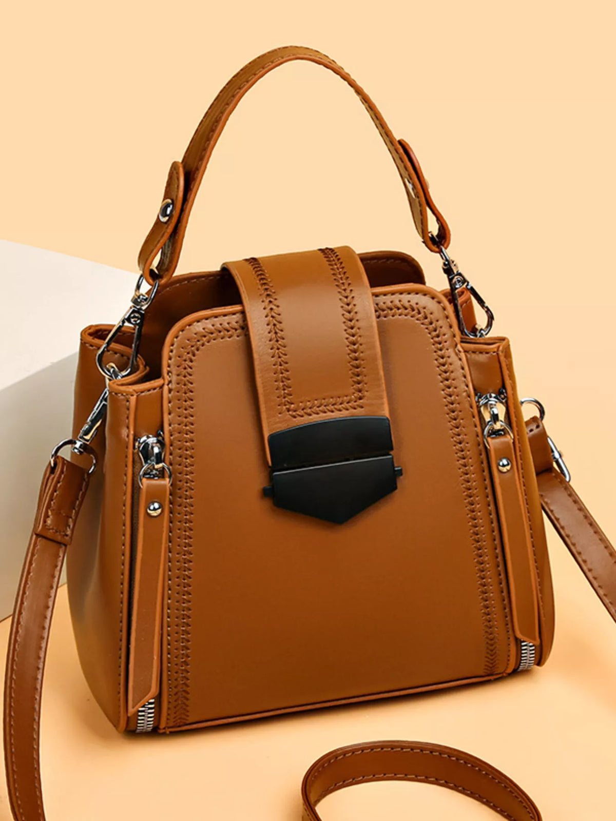 Medium tan PU leather crossbody bag with a structured silhouette, top handle, stitched panels, detachable straps, silver hardware, and a black front clasp.