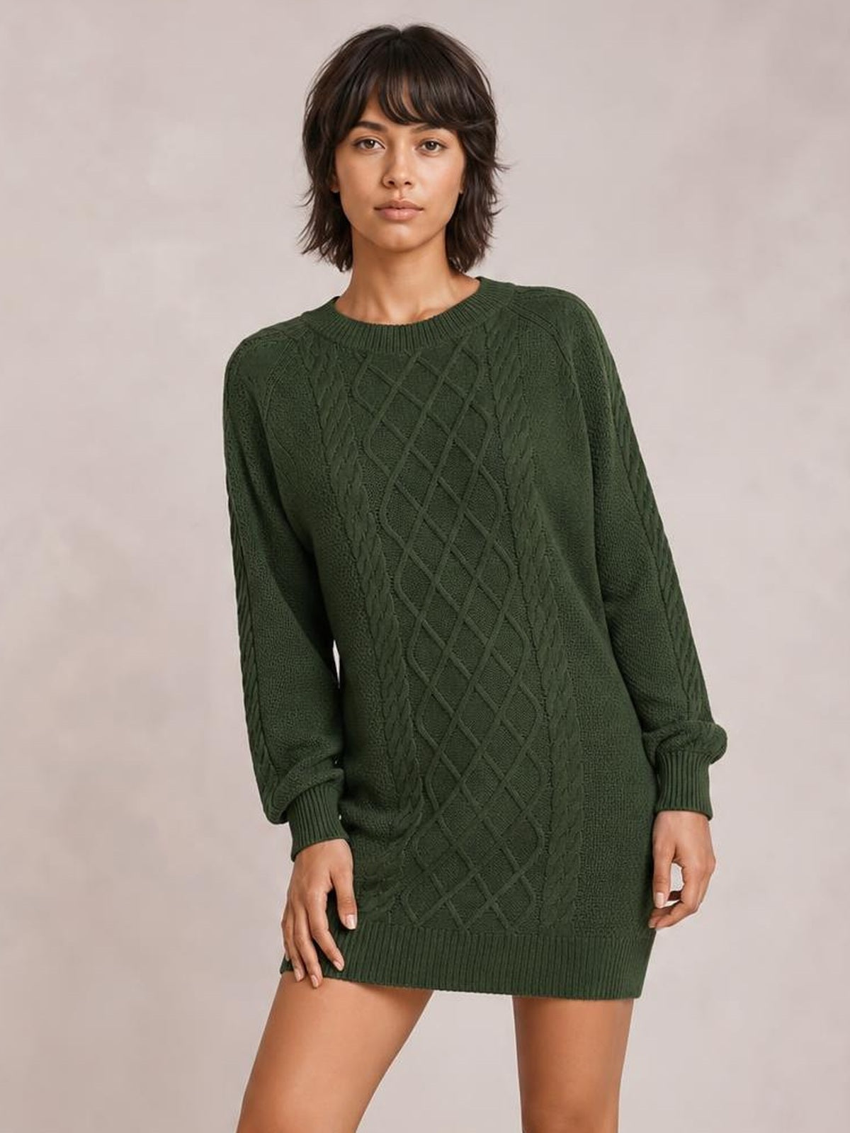 Model poses in a dark green diamond cable-knit sweater dress with long sleeves, ribbed crew neckline, cuffs, and hem in a relaxed silhouette.