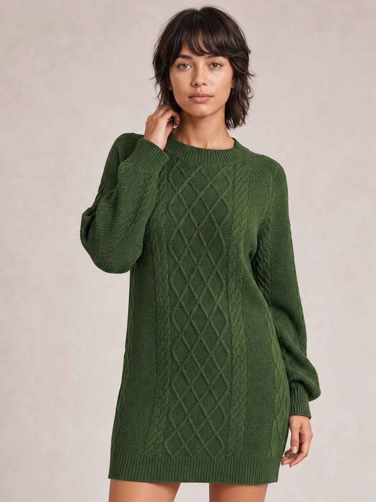 Model poses with one hand at her neck, wearing a forest-green diamond cable-knit sweater dress with long sleeves, ribbed crew neck, cuffs, and hem.