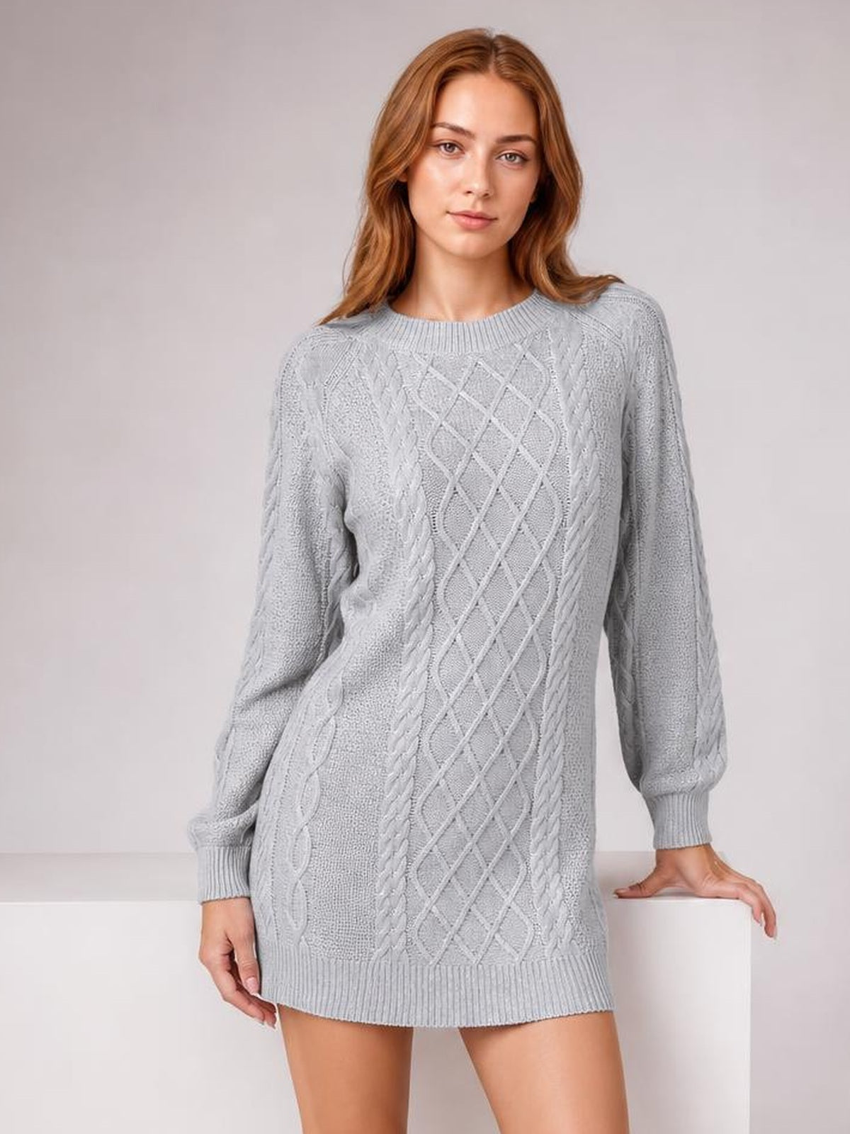 Model in a light gray diamond cable-knit sweater dress with long sleeves, ribbed crew neckline and hem, and a relaxed thigh-length silhouette.