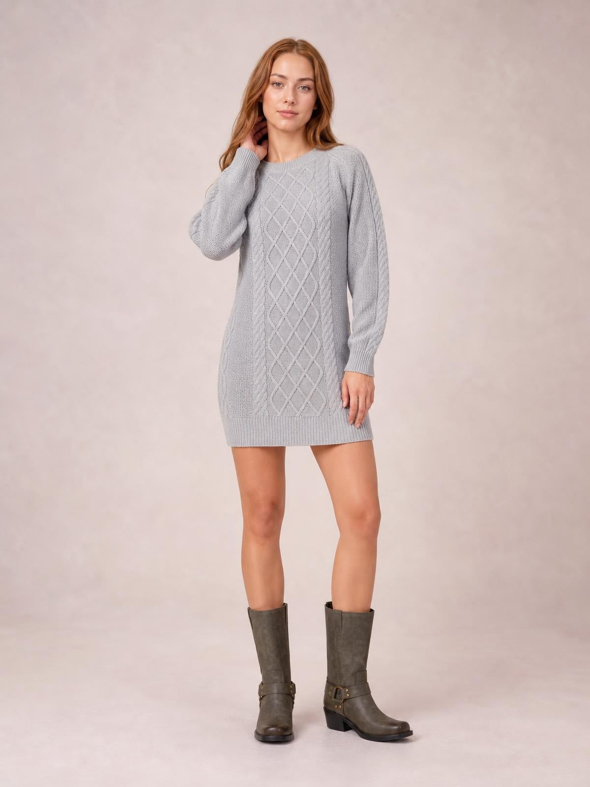 Model poses in a light gray diamond cable-knit sweater dress with long sleeves, ribbed cuffs and hem, and a straight mini-length silhouette.