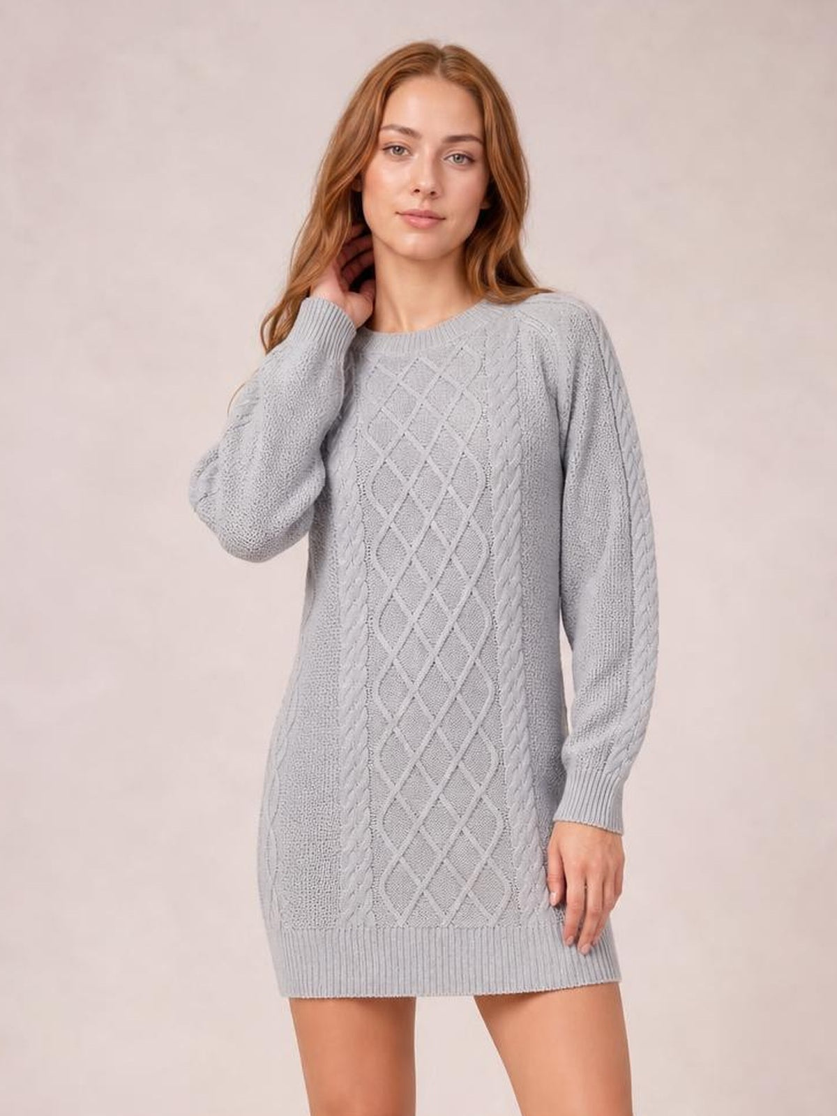 Model wearing a light gray diamond cable-knit sweater dress with long sleeves, ribbed crew neckline and hem, relaxed straight silhouette, and one hand touching her neck.