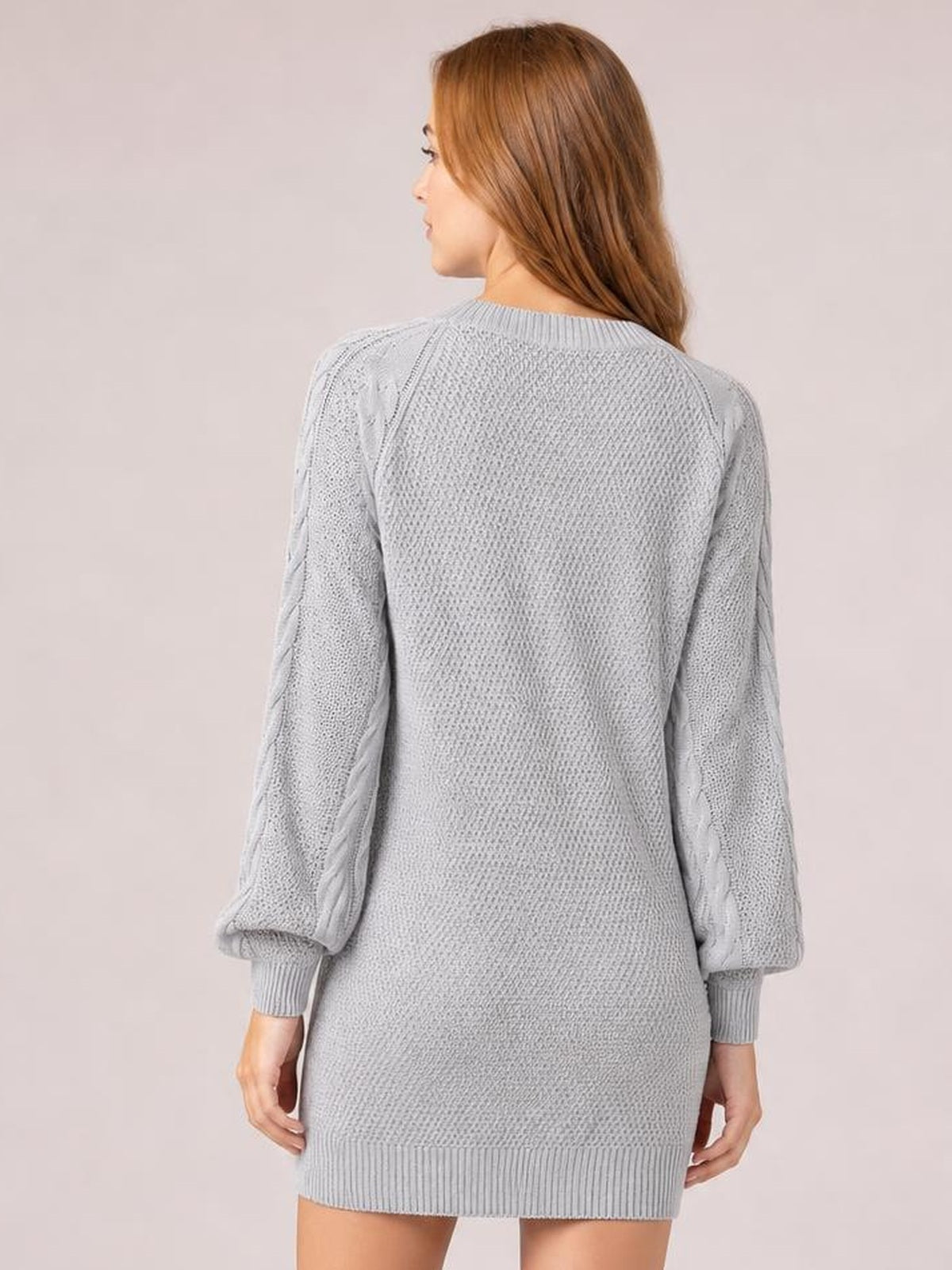 A model poses facing away in a light gray diamond cable-knit sweater dress with long sleeves, a relaxed silhouette, and ribbed cuffs and hem.