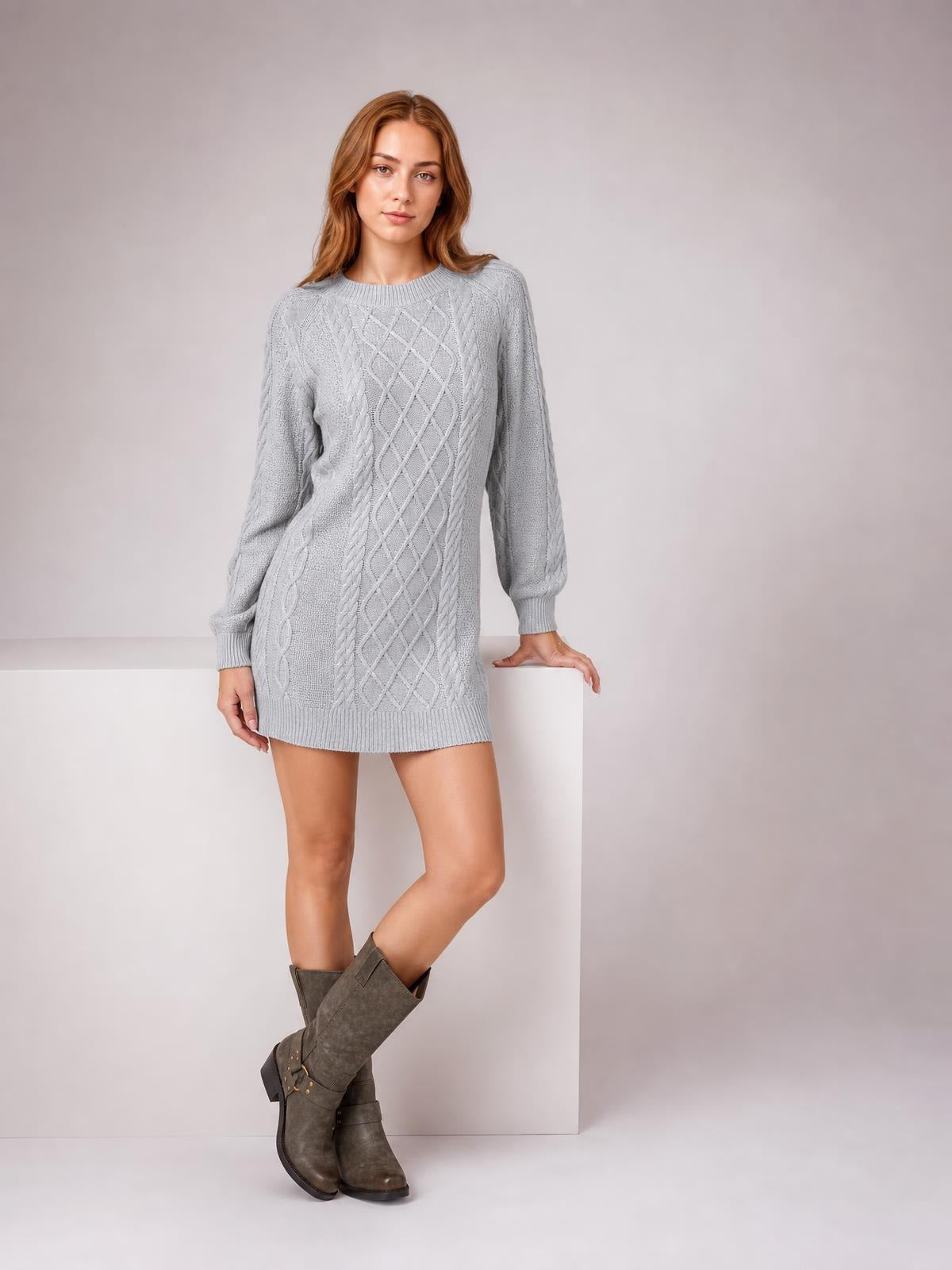 Model wears a light gray diamond cable-knit sweater dress with long sleeves, ribbed trim, a straight relaxed silhouette, and crossed legs.