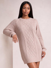 Model in a soft blush diamond cable-knit sweater dress with long sleeves, ribbed crew neckline, cuffs, and hem, shown in a relaxed leaning pose.