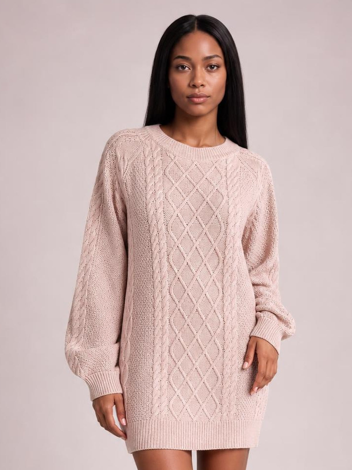 Model stands facing forward in a pale pink diamond cable-knit sweater dress with long sleeves, ribbed crew neckline, cuffs, and hem.