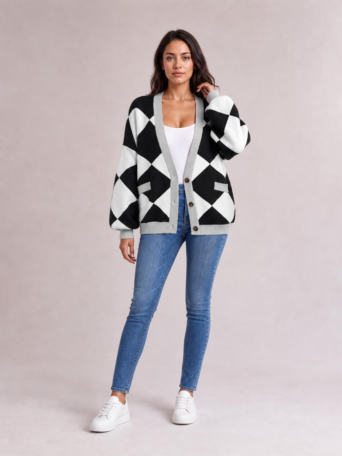 Model poses in a black-and-white diamond pattern button-up knit cardigan with gray trim, ribbed cuffs and hem, front pockets, and a relaxed silhouette.