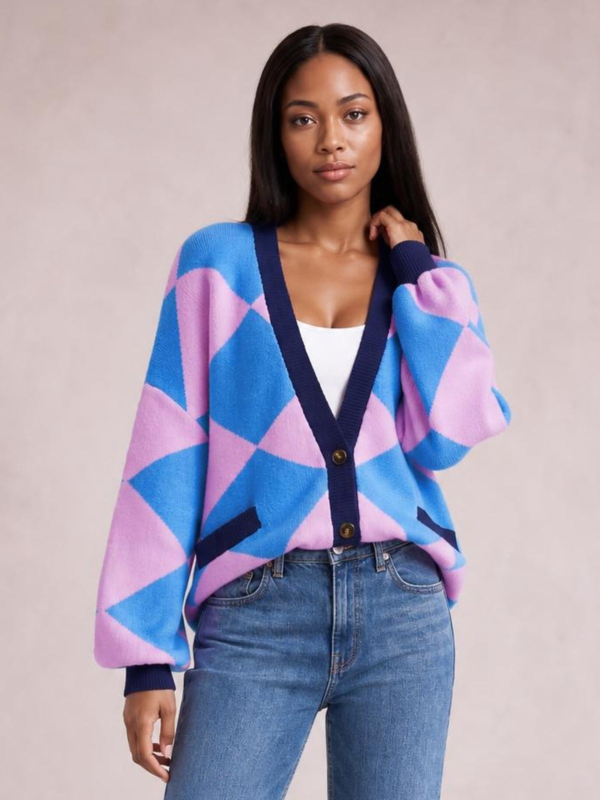 A model wears a blue and pink diamond-pattern button-up knit cardigan with a V-neck, long sleeves, front pockets, and a relaxed silhouette.