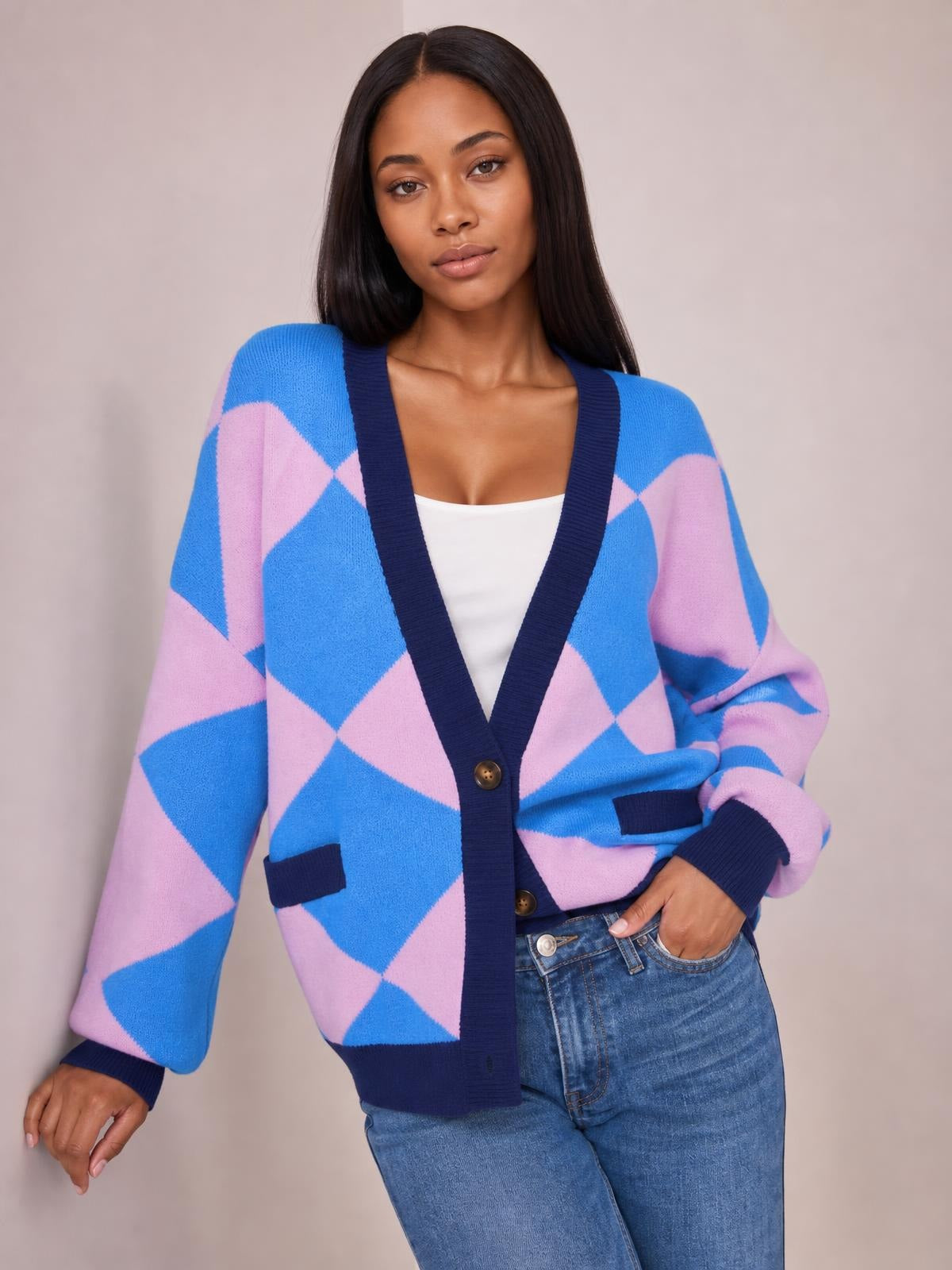 Model poses in a blue and pink diamond pattern button-up knit cardigan with navy ribbed trim, long sleeves, front pockets, and a relaxed silhouette.