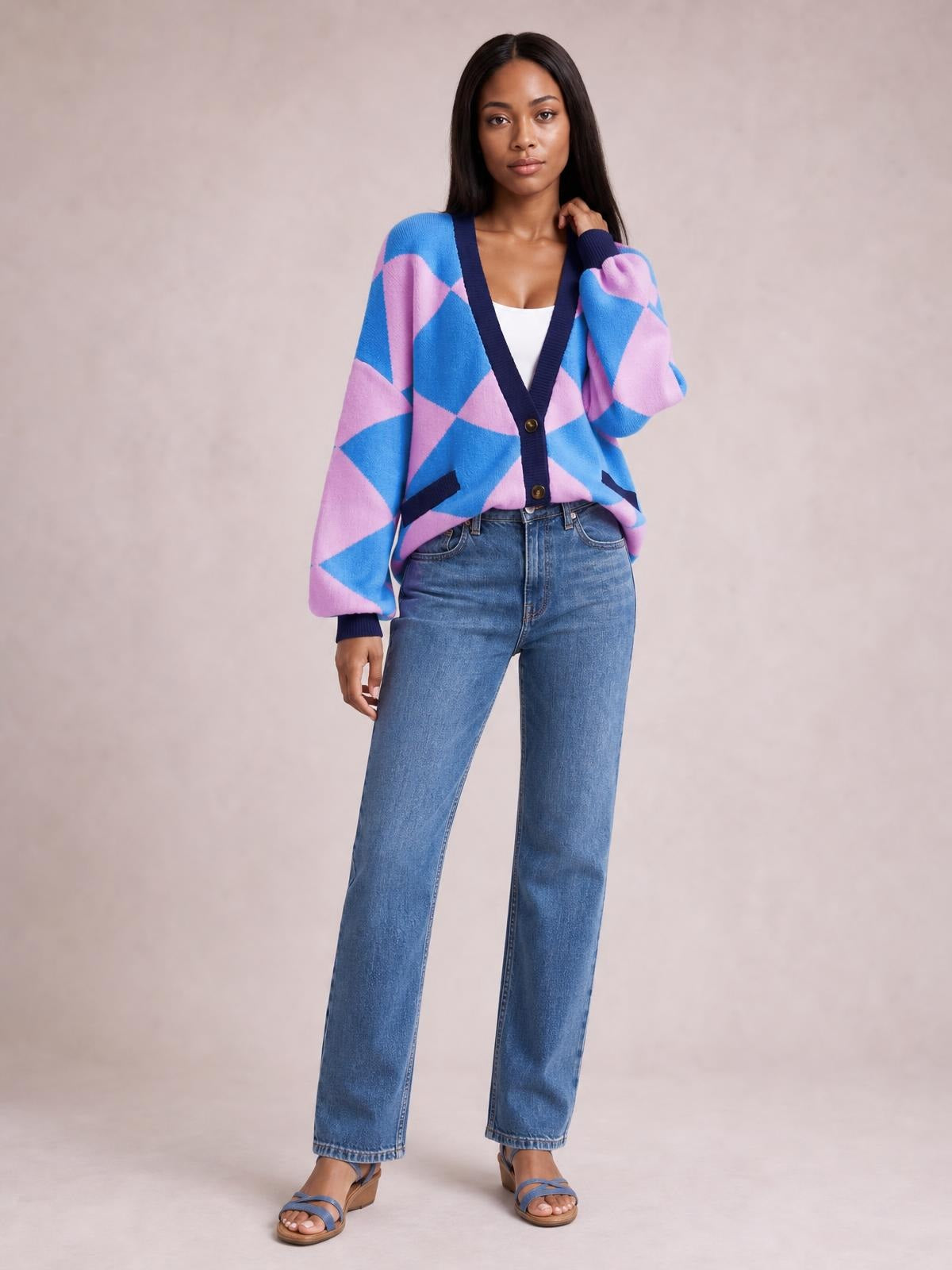 A model stands in a blue and pink diamond pattern button-up knit cardigan with a V-neck, contrasting trim, front pockets, and relaxed sleeves.