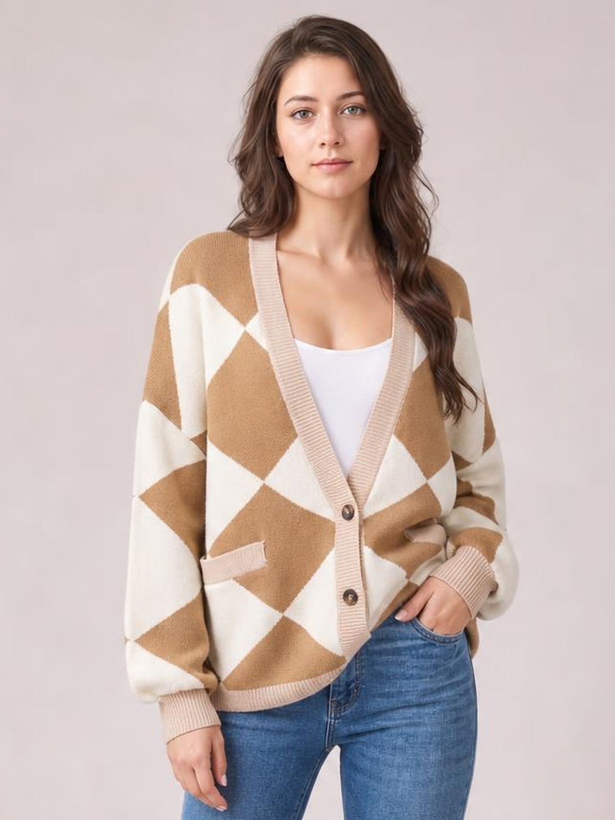 Model poses in a tan and cream diamond pattern button-up knit cardigan with ribbed trim, long sleeves, front pockets, and a relaxed silhouette.
