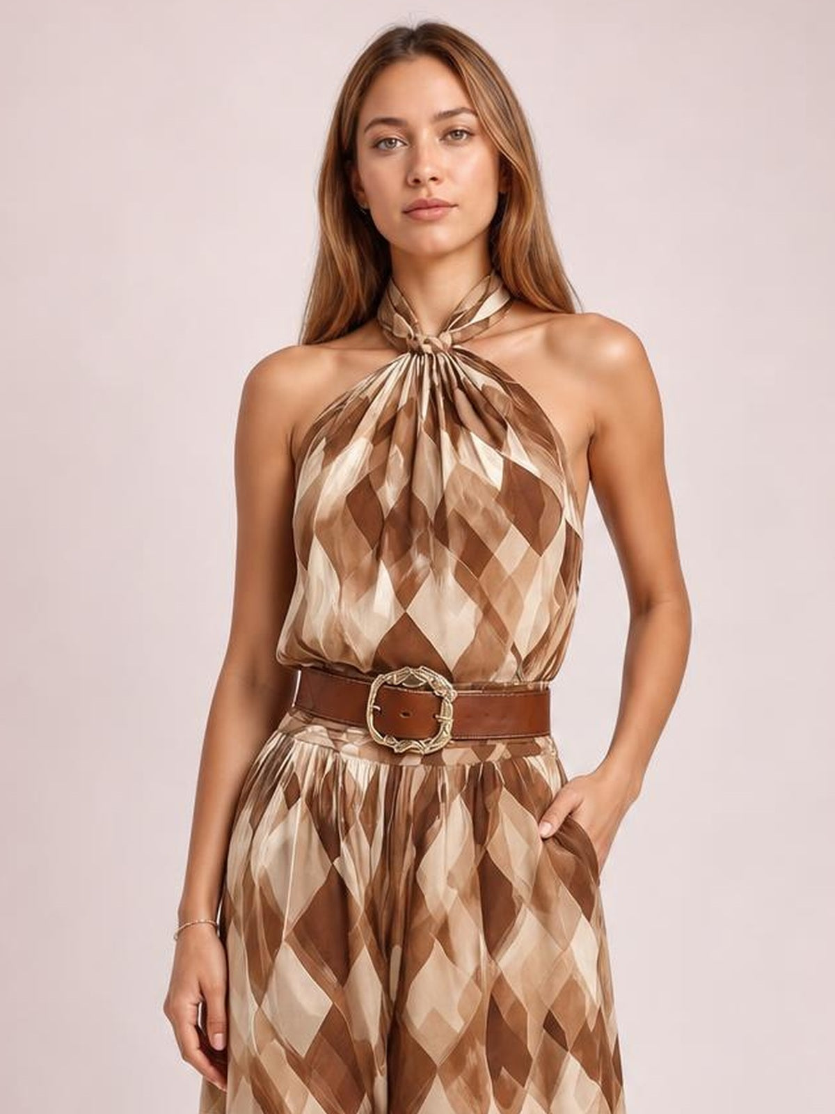 A model poses in a brown and cream diamond-pattern halter-neck maxi dress with a twisted gathered neckline, flowing silhouette, and wide belt.