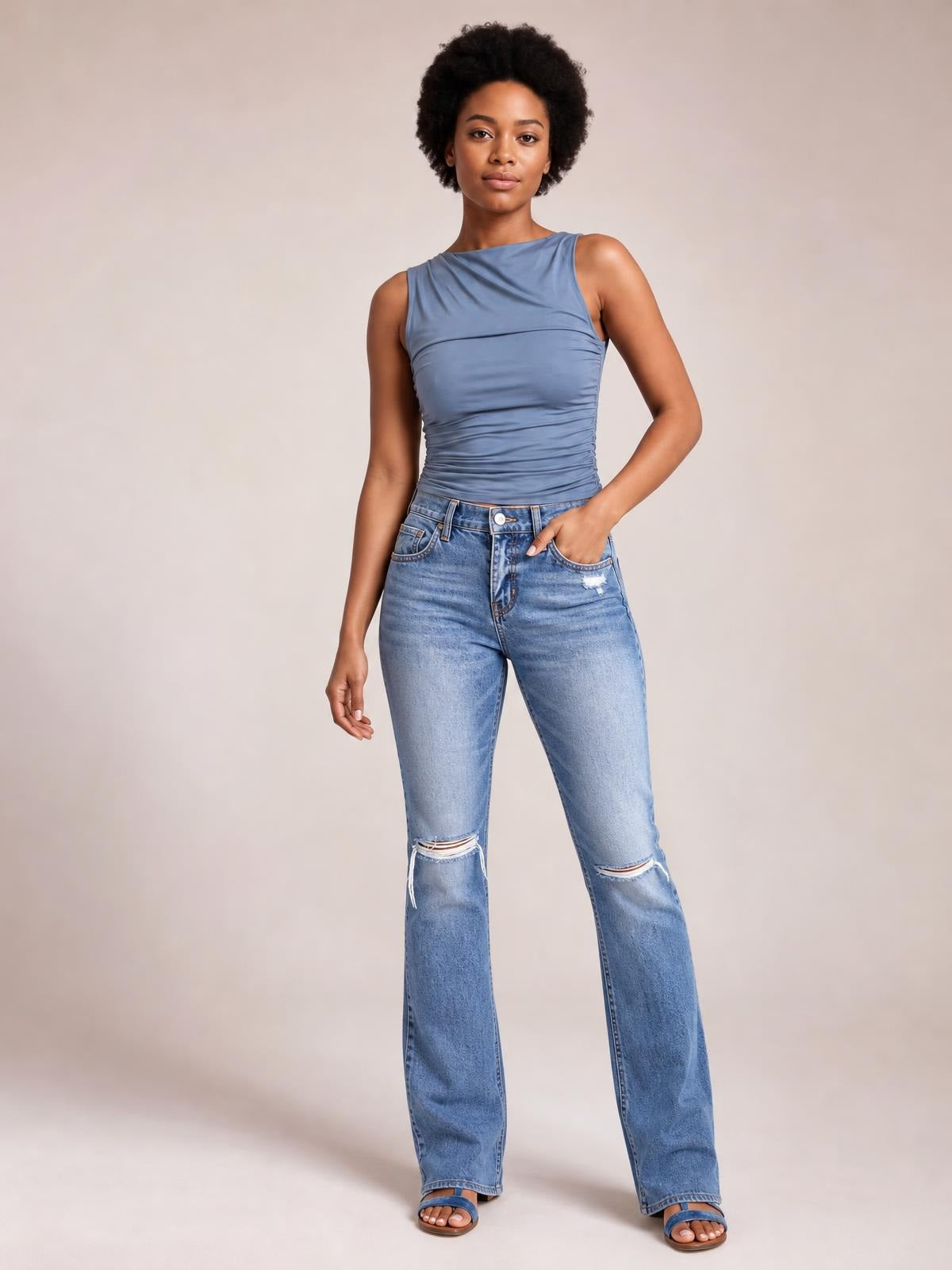 Model poses in light blue distressed flare jeans with a button fly, front pockets, ripped knees, and a fitted hip-to-flared-leg silhouette.