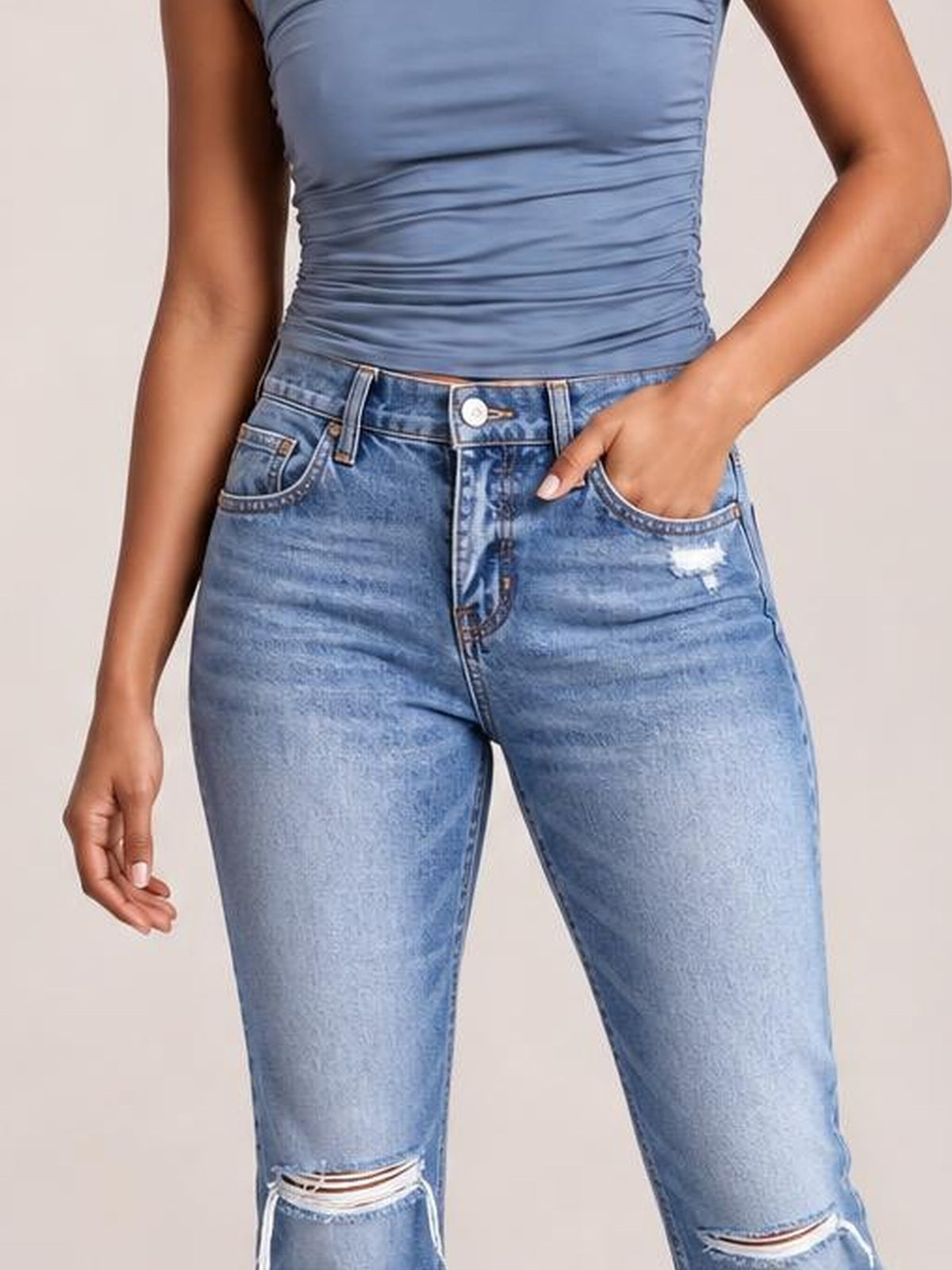 A model wears light-wash distressed flare jeans with a button closure, belt loops, front pockets, and ripped knees, posing with one hand in a pocket.