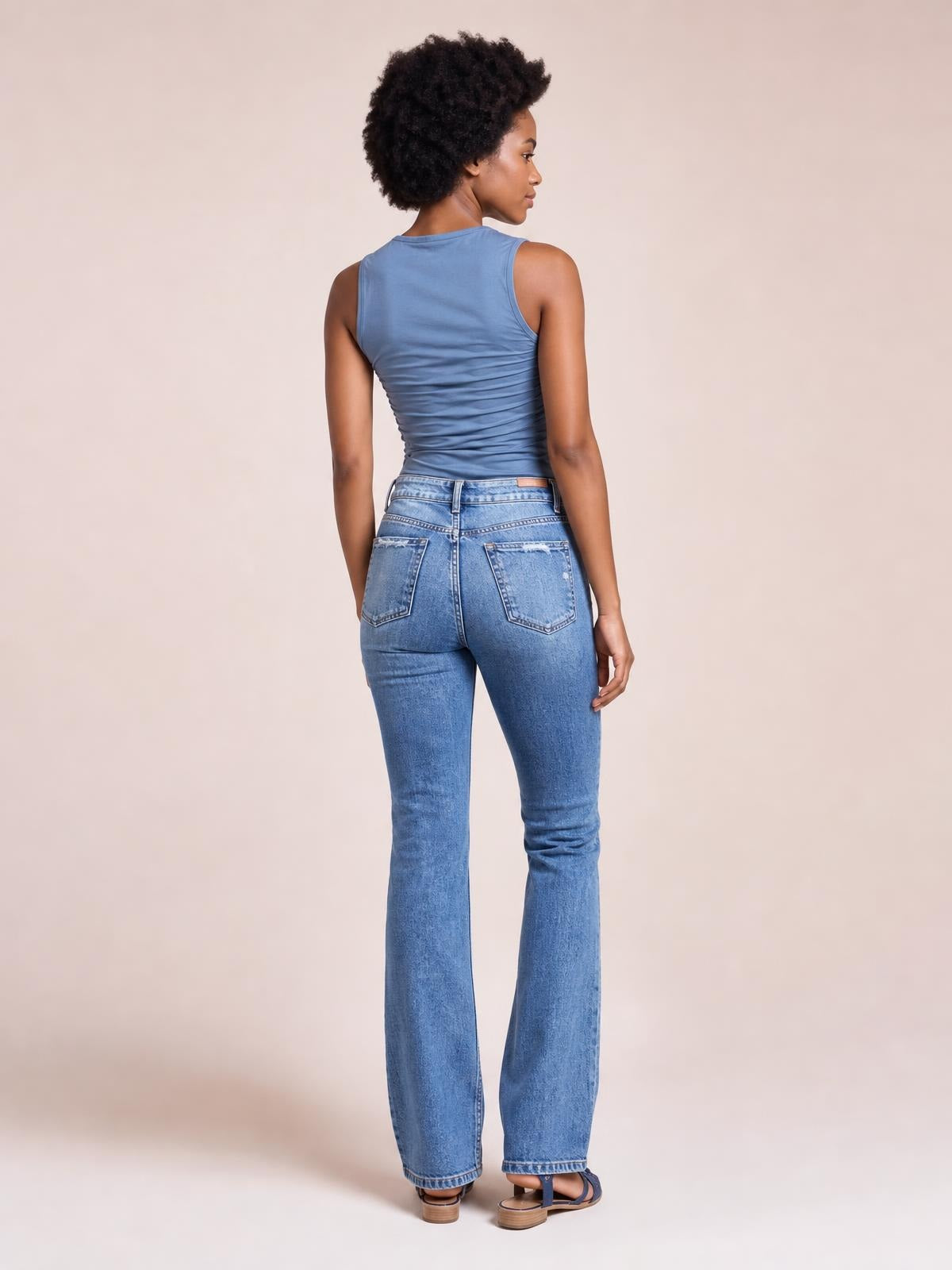 A model poses from the back in light blue distressed flare jeans with a fitted waist and hips, belt loops, back pockets, and gently flared legs.