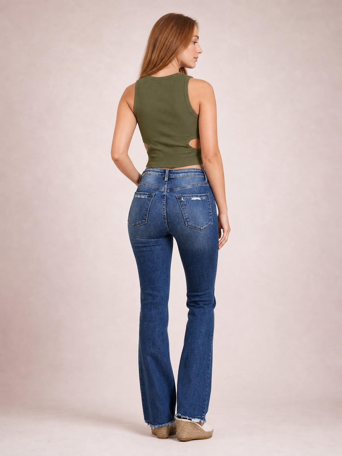Model poses from the back in blue distressed flare jeans with a fitted silhouette, button closure, belt loops, and two back pockets.