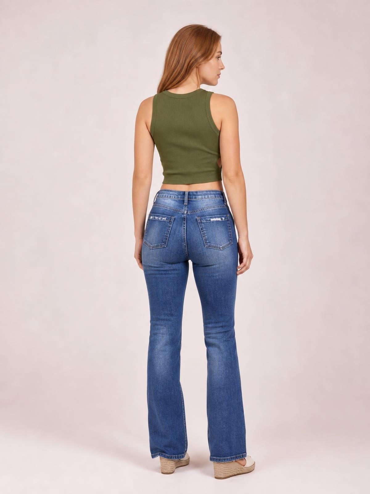 Model shown from the back in blue distressed flare jeans with buttoned back pockets, a fitted waist and thighs, and wide flared legs.