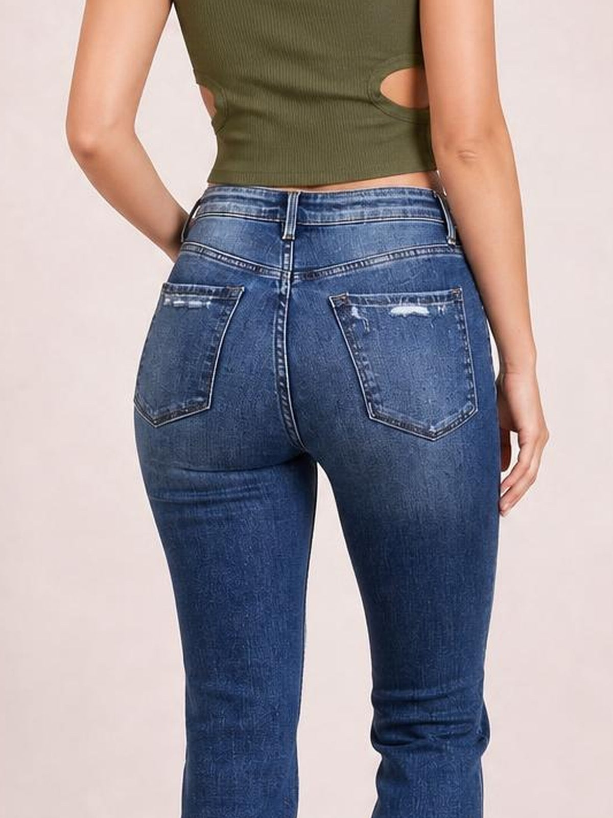 A model poses from behind in dark blue distressed flare jeans with a fitted seat, belt loops, contrast stitching, and two back patch pockets.