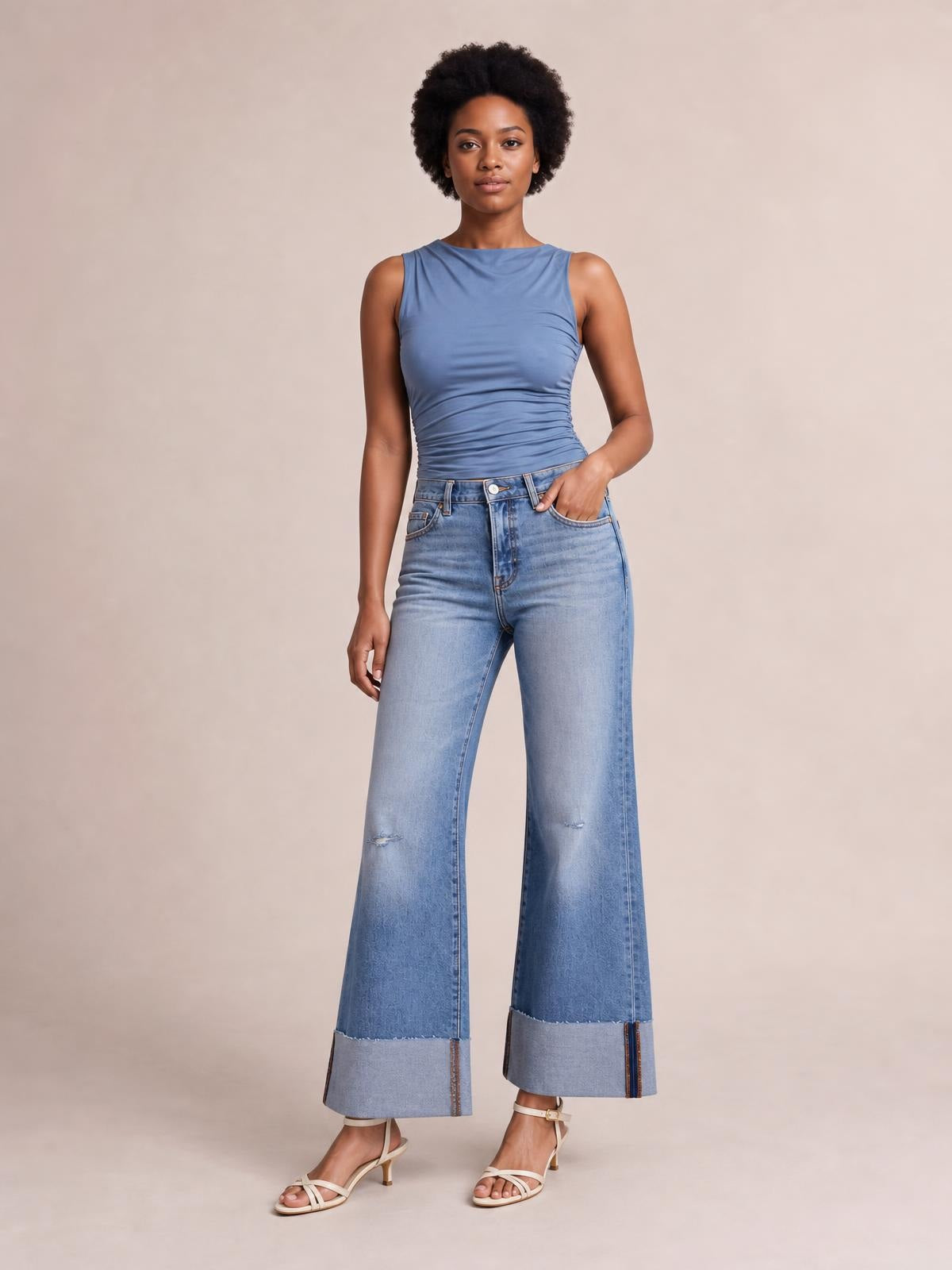 Model wears light-wash distressed high-waisted flare jeans with a fitted hip, wide-leg silhouette, knee tears, five-pocket construction, and raw hems.