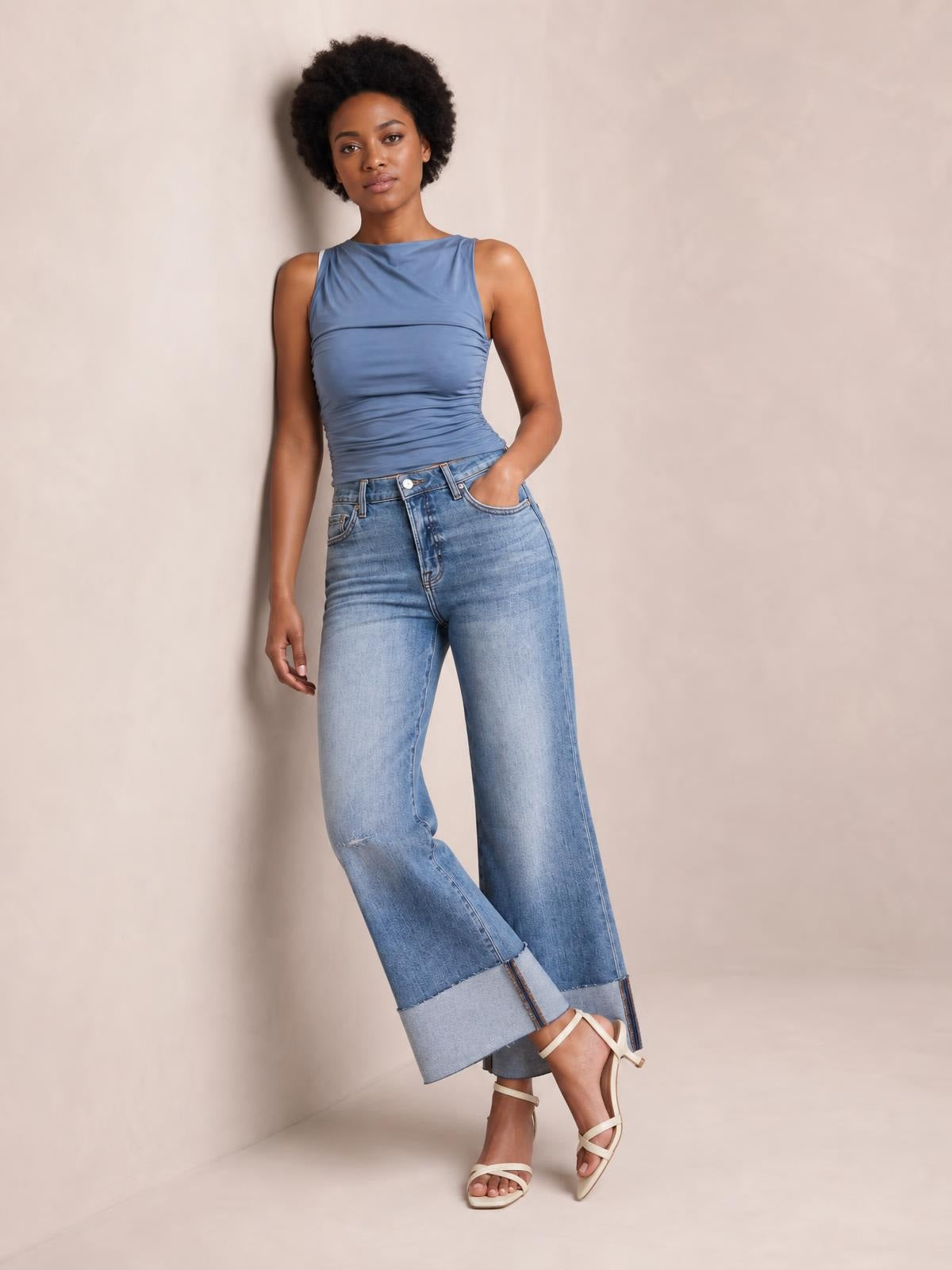 Model poses with one hand in the pocket, wearing light-wash distressed high-waisted flare jeans with a fitted hip, wide legs, and raw hems.