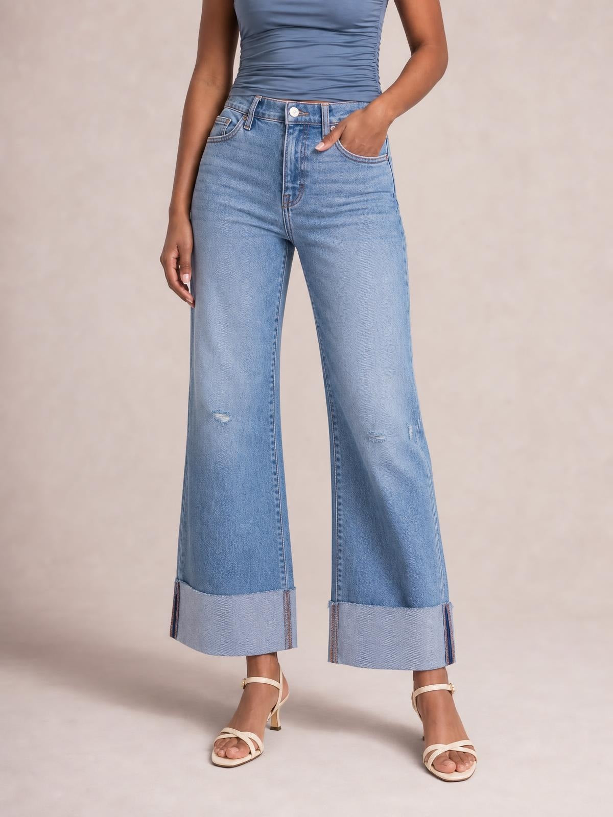 A model stands in light-blue distressed high-waisted flare jeans with five-pocket construction, wide legs, small abrasions, and oversized turned-up raw hems.