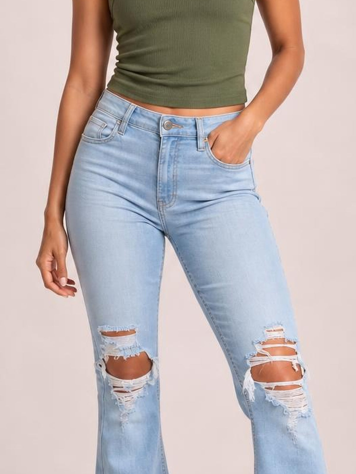 Model poses in light blue distressed jeans with button closure, belt loops, front pockets, a fitted silhouette, and heavily ripped knees.
