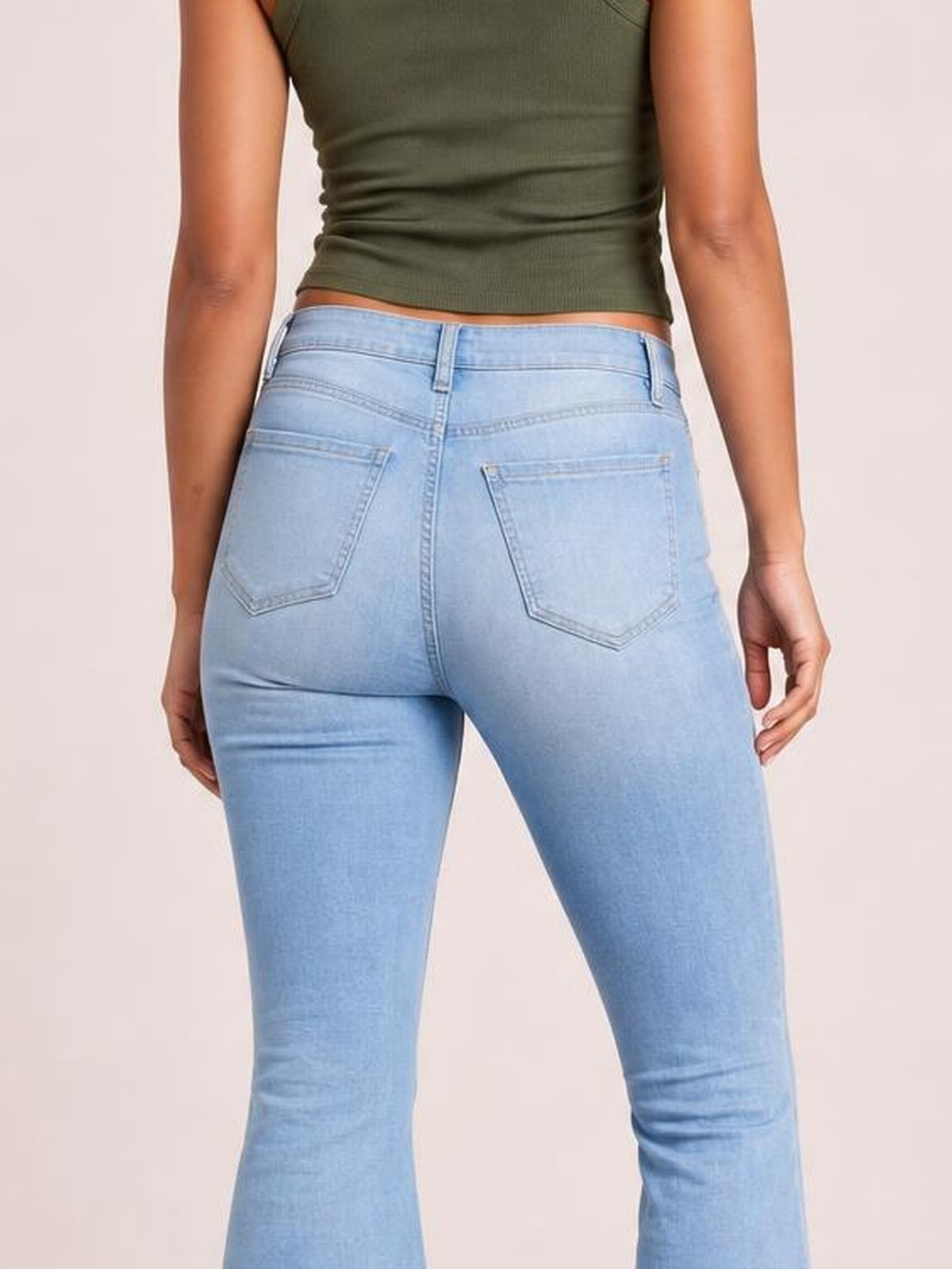 Model shown from behind wearing light blue distressed jeans with a fitted silhouette, belt loops, buttoned waistband, and two stitched back pockets.