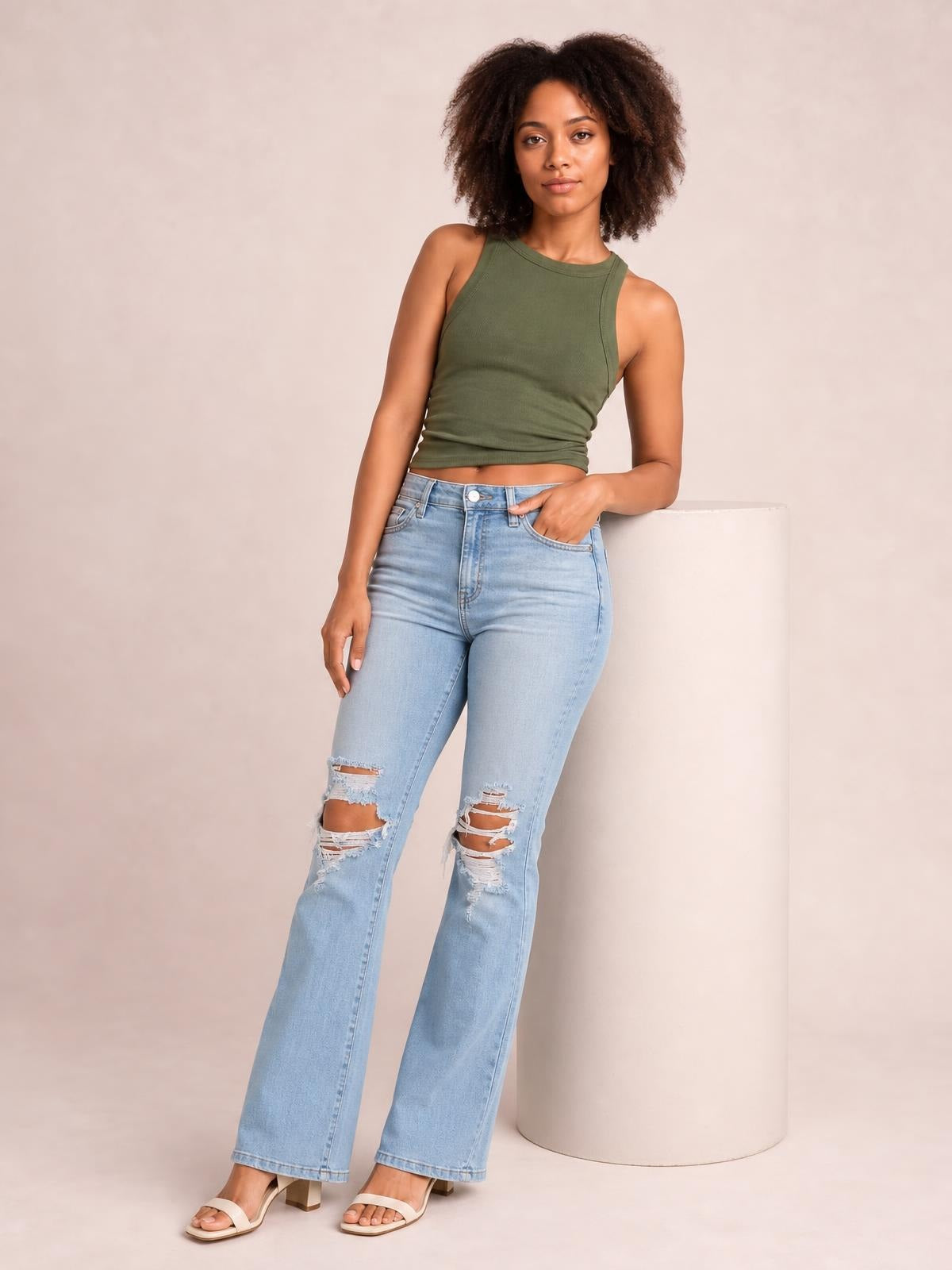 Model poses in light-wash distressed jeans with visible pockets, button closure, a fitted high waist, and a long straight-leg silhouette.
