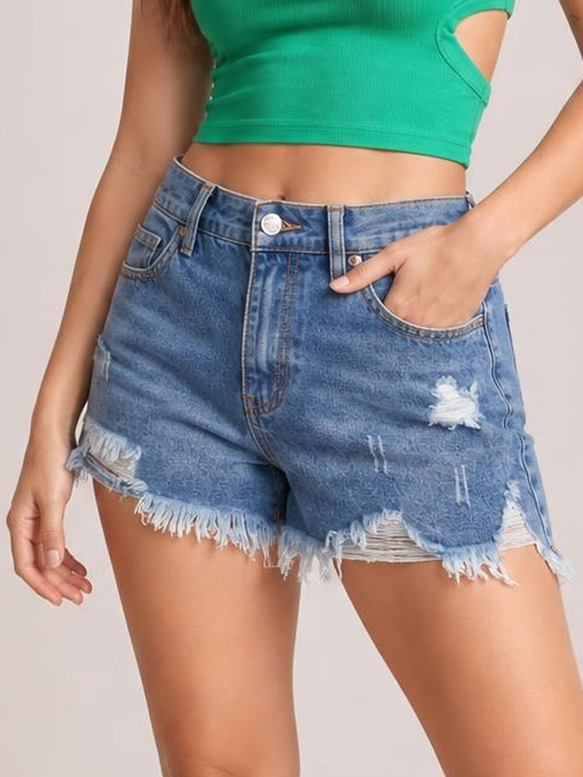 Model wears blue distressed raw hem denim shorts with a button fly, belt loops, front pockets, ripped details, and a relaxed silhouette.