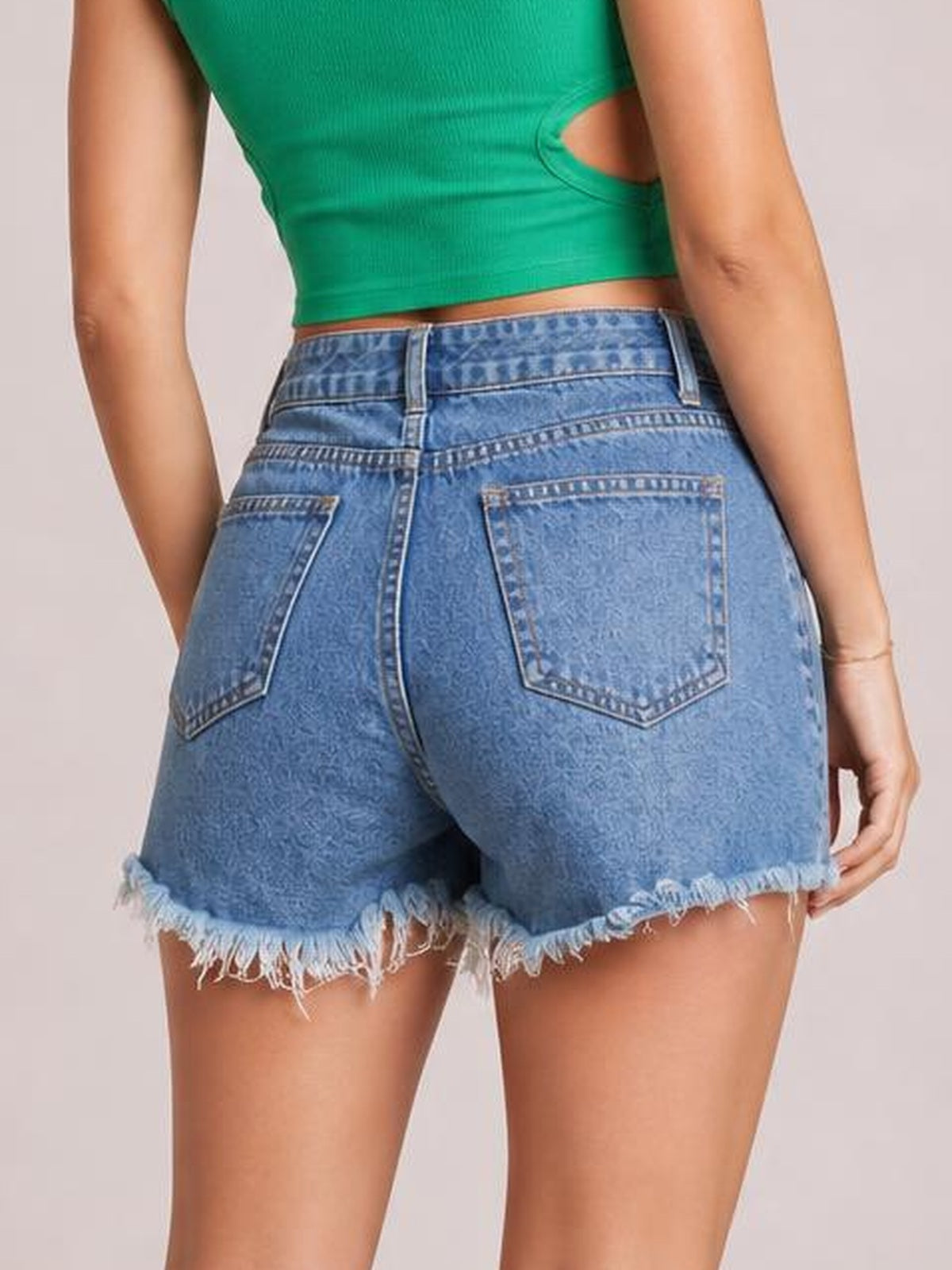A model poses from the back wearing blue distressed raw hem denim shorts with a structured waistband, belt loops, and two back patch pockets.