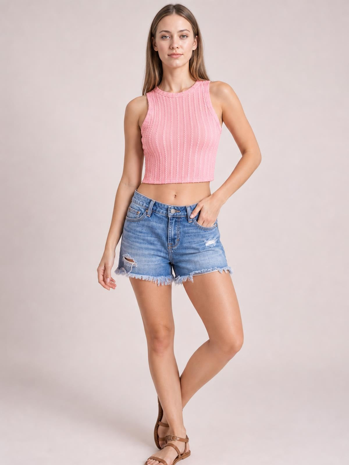 Model poses with one hand in the pocket of light blue distressed raw hem denim shorts, featuring front pockets, button closure, ripped details, and a relaxed silhouette.