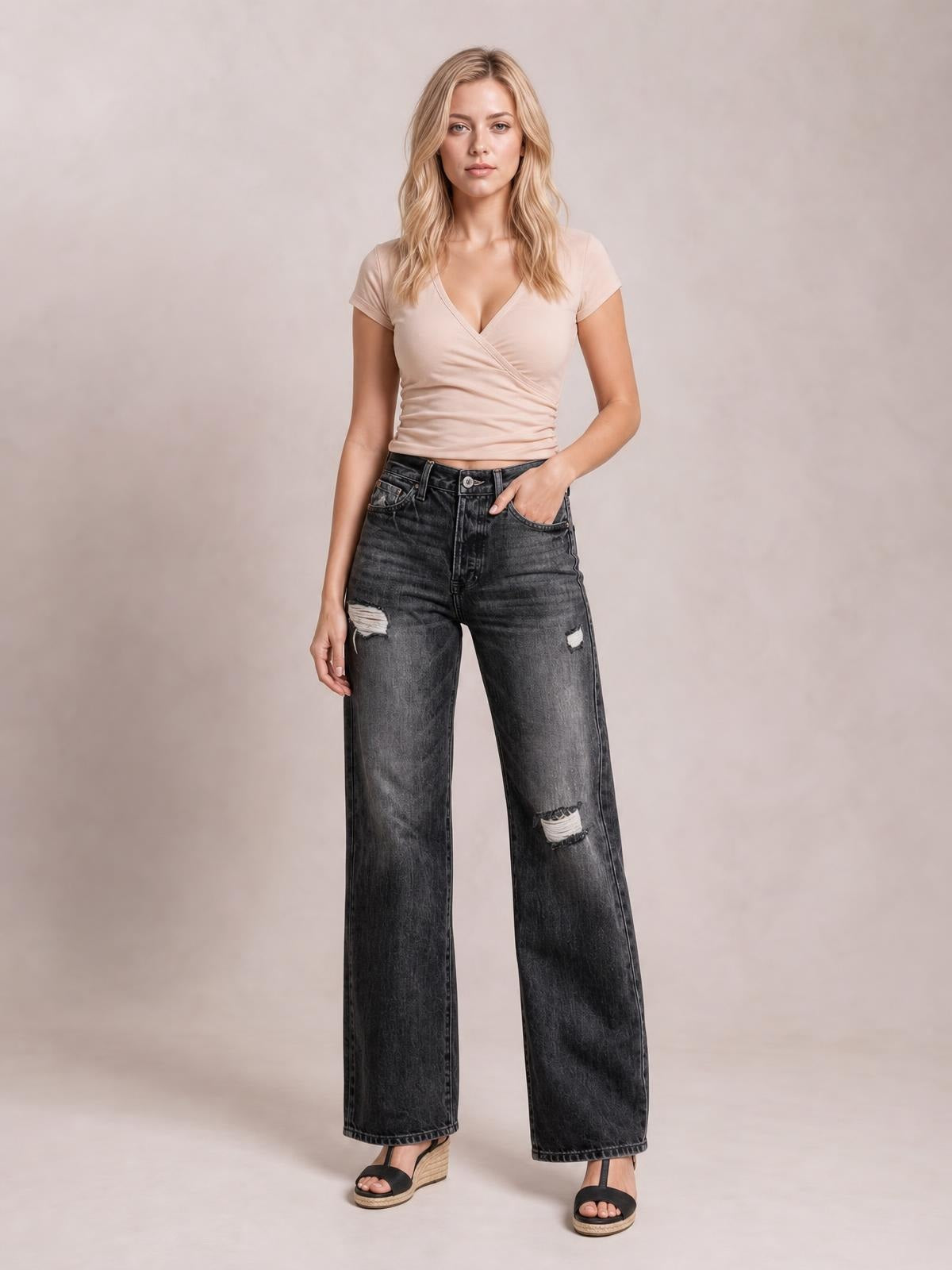 Model poses in dark gray distressed straight leg jeans with a high-rise fit, front pockets, button closure, and ripped details at the thighs and knee.